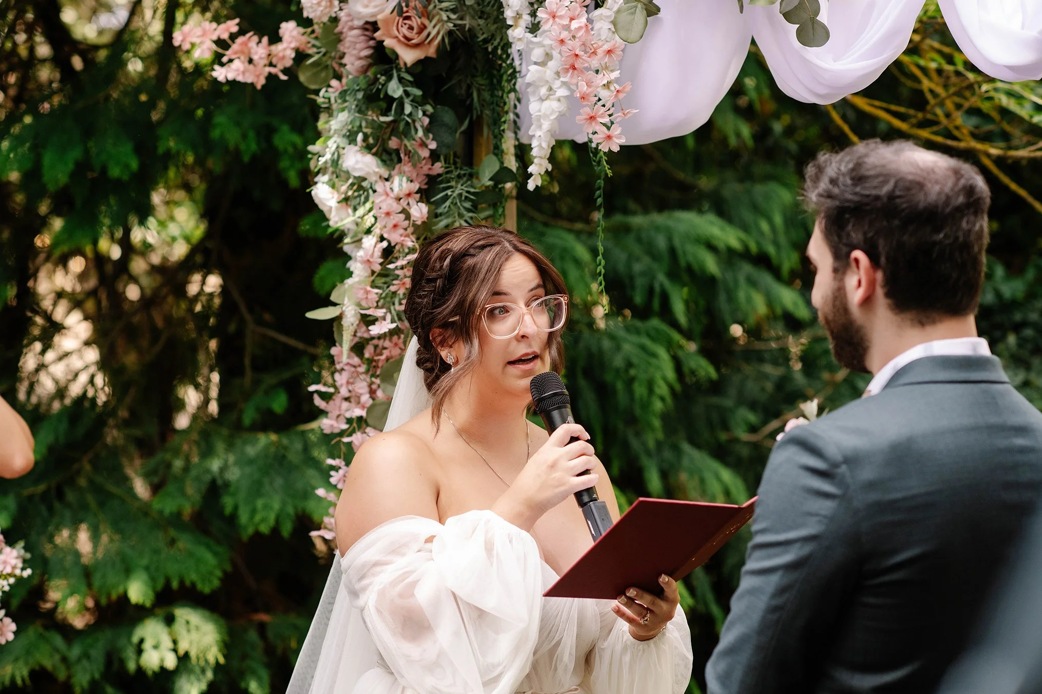 bride looks at groom as she reads her vows under flower arbor at Chateau Dore