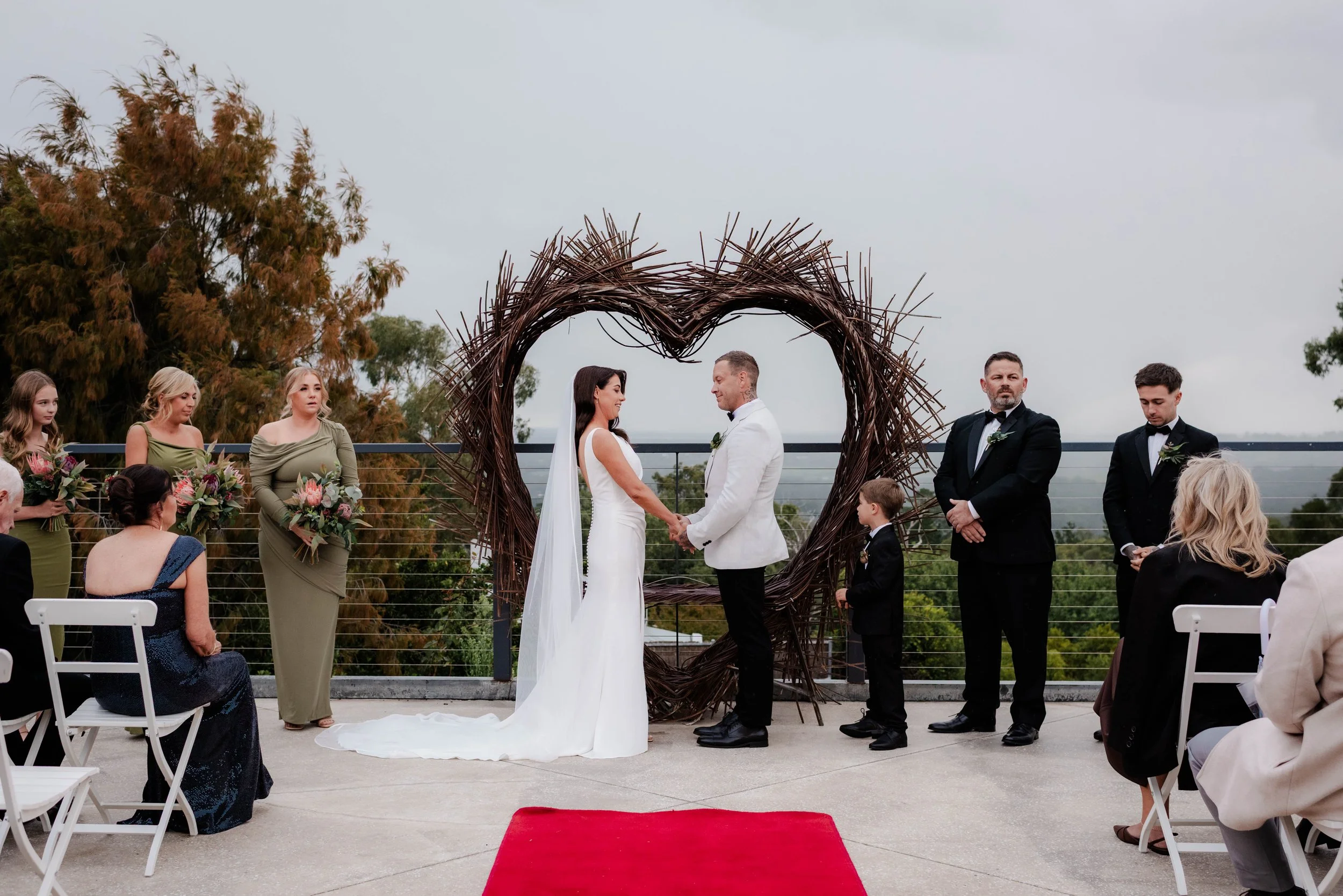Wide view of outdoor wedding ceremony with bride and groom holding hands under a twig arch at Jason's Restaurant Beaconsfield Victoria