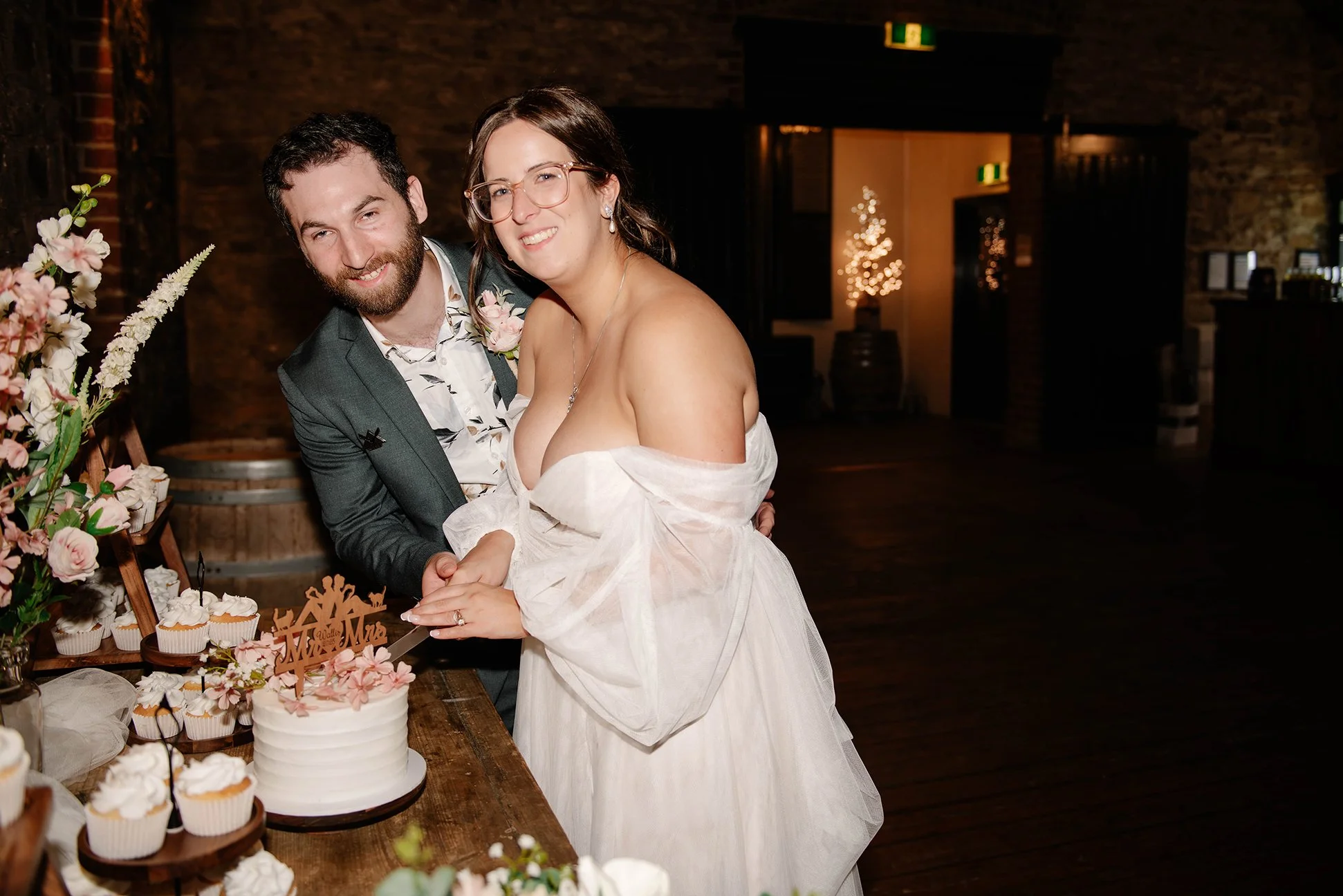 bride and groom look at camera and cut wedding cake at wedding reception in Bendigo