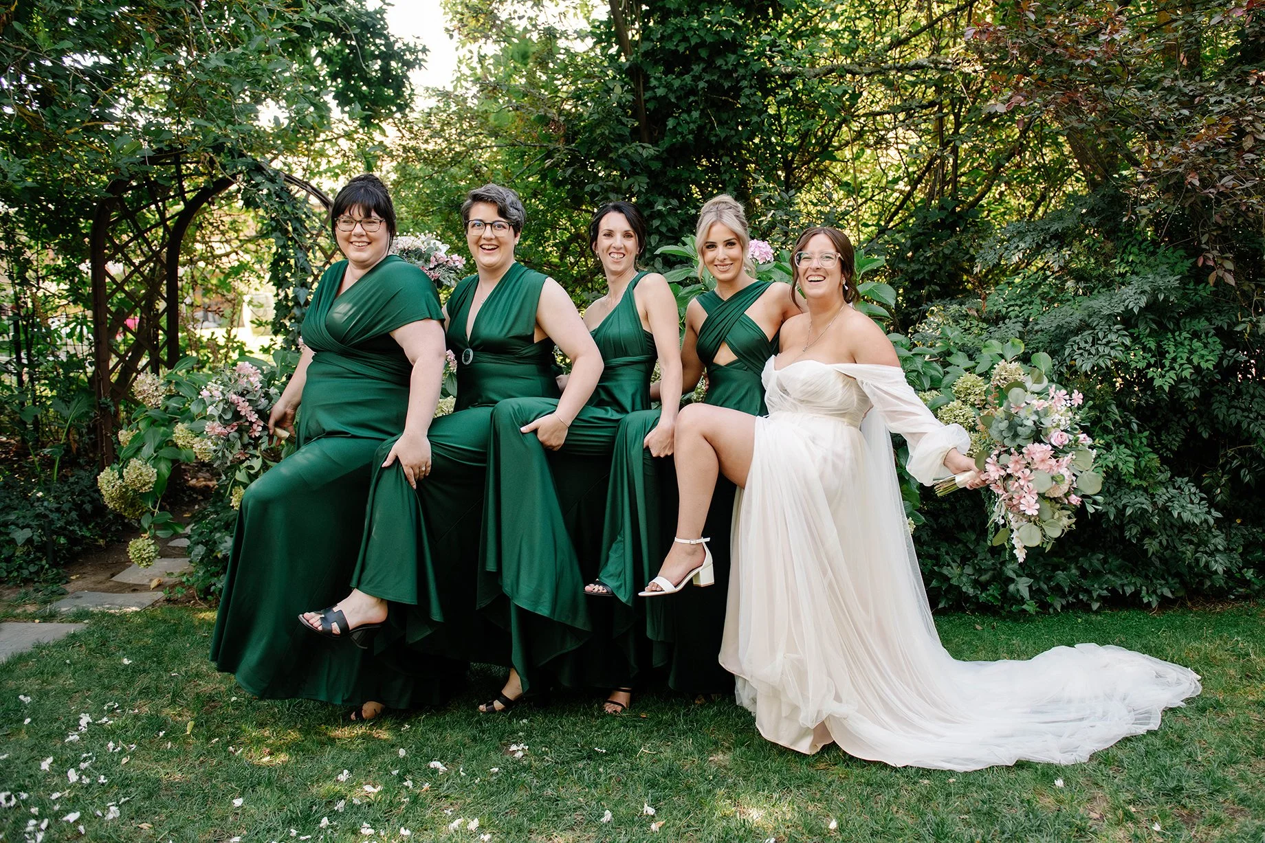 bridal party in green dresses with bride do funny pose holding each others raised leg in Bendigo