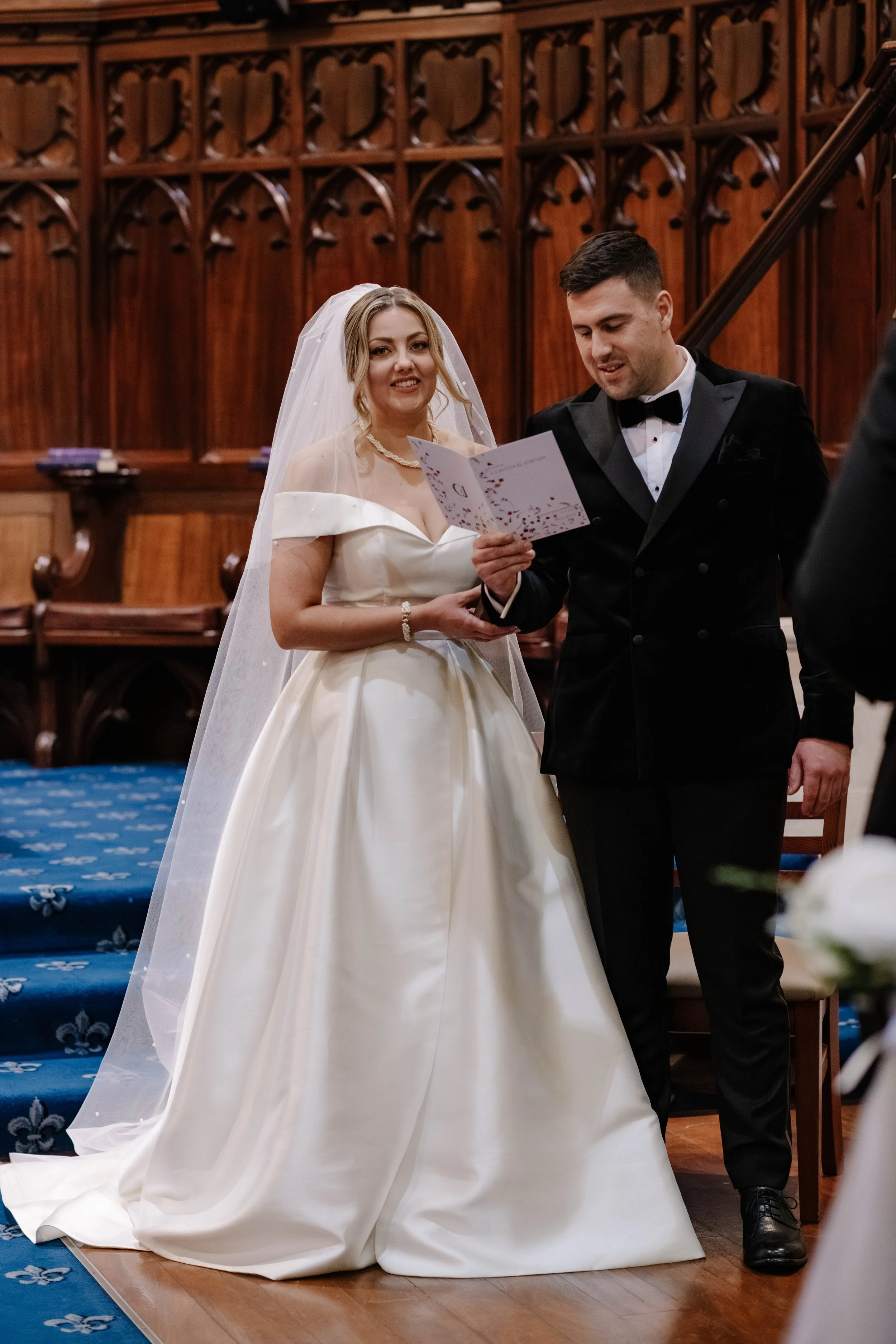 bride and groom stand together as bride smiles at camera and they read from their church service