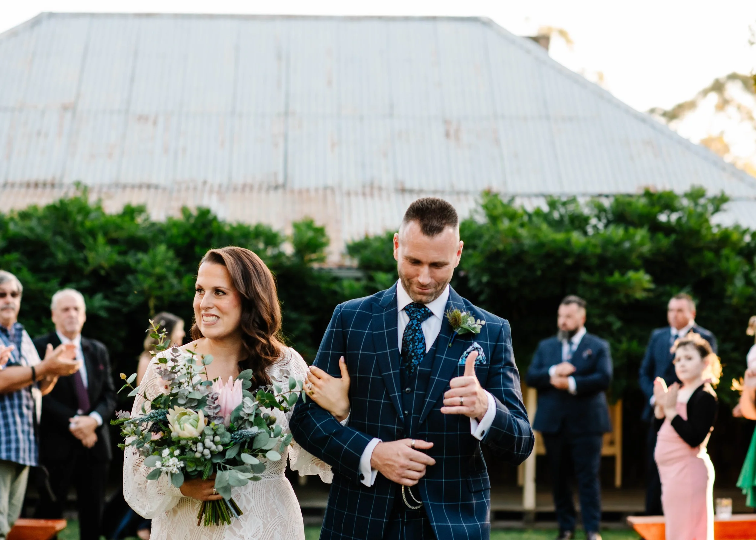 Bride and groom walking back up the aisle after their outdoor wedding ceremony in front of a rustic corrugated iron barn at Sage's Cottage Victoria