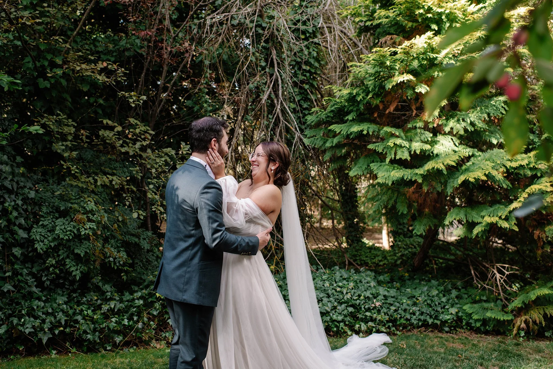 bride holding grooms face and smiling as he embraces her in well lit garden at Chateau Dore in Bendigo