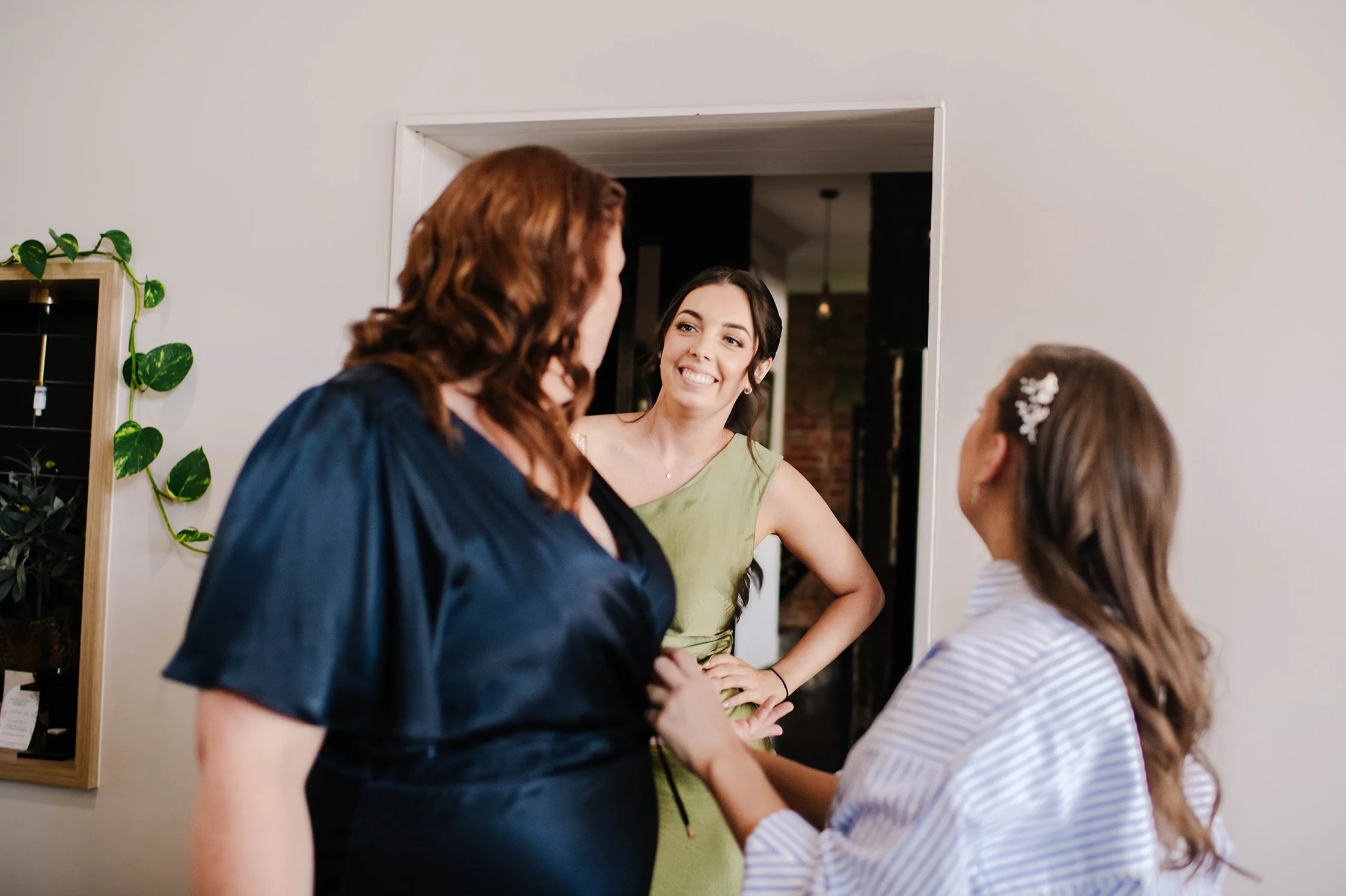 Bridesmaid smiles as mother of bride and bride look at her