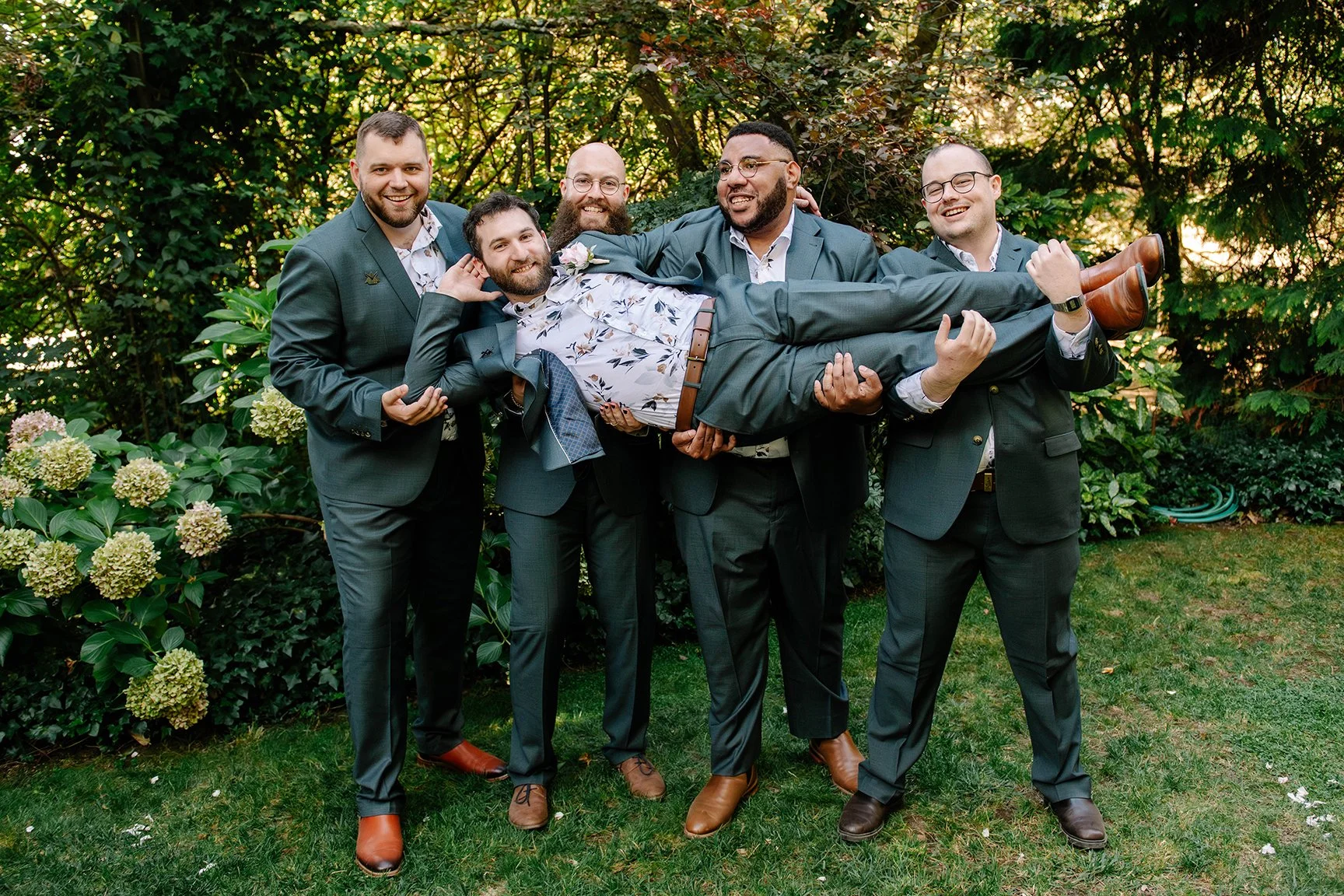 groomsmen hold groom in air vertically as he holds his head in his hand in green Chateau Dore garden Bendigo