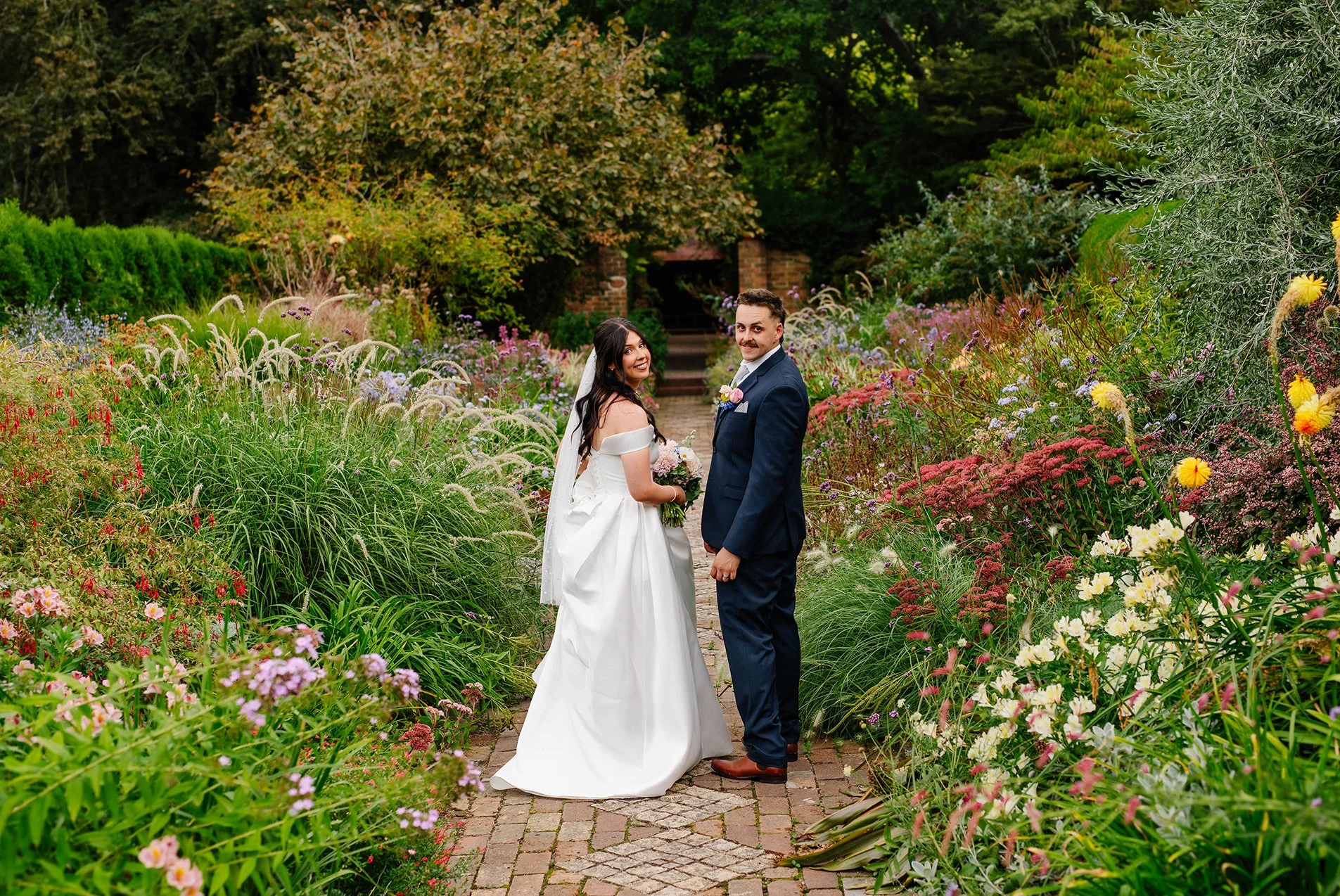 Bride and groom smile and look back at the camera as they casually walk through the wildflower garden at Cloudehill Olinda