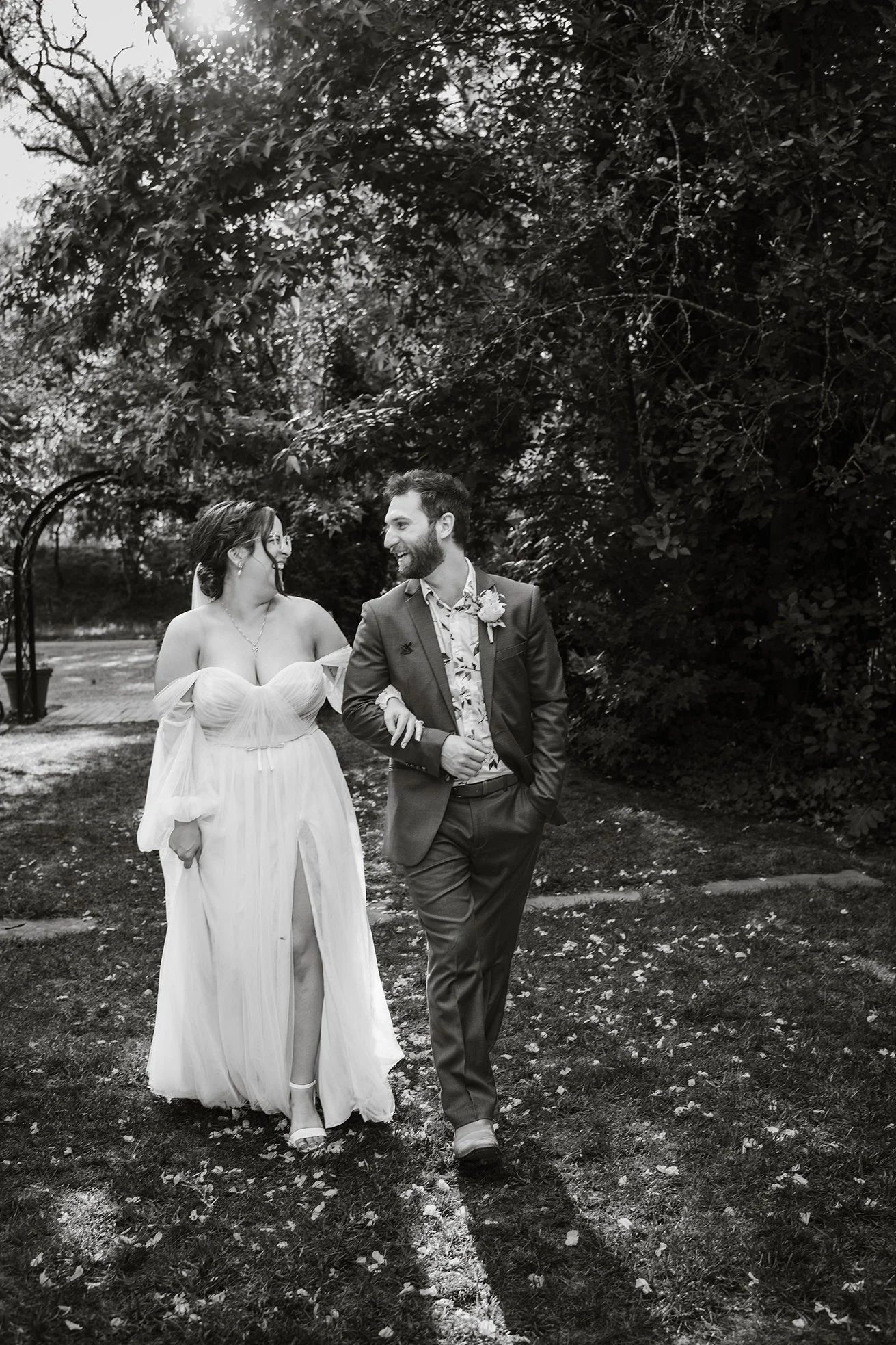 Black and white shot of bride and groom arm in arm walking through Chateau Dore garden in Bendigo