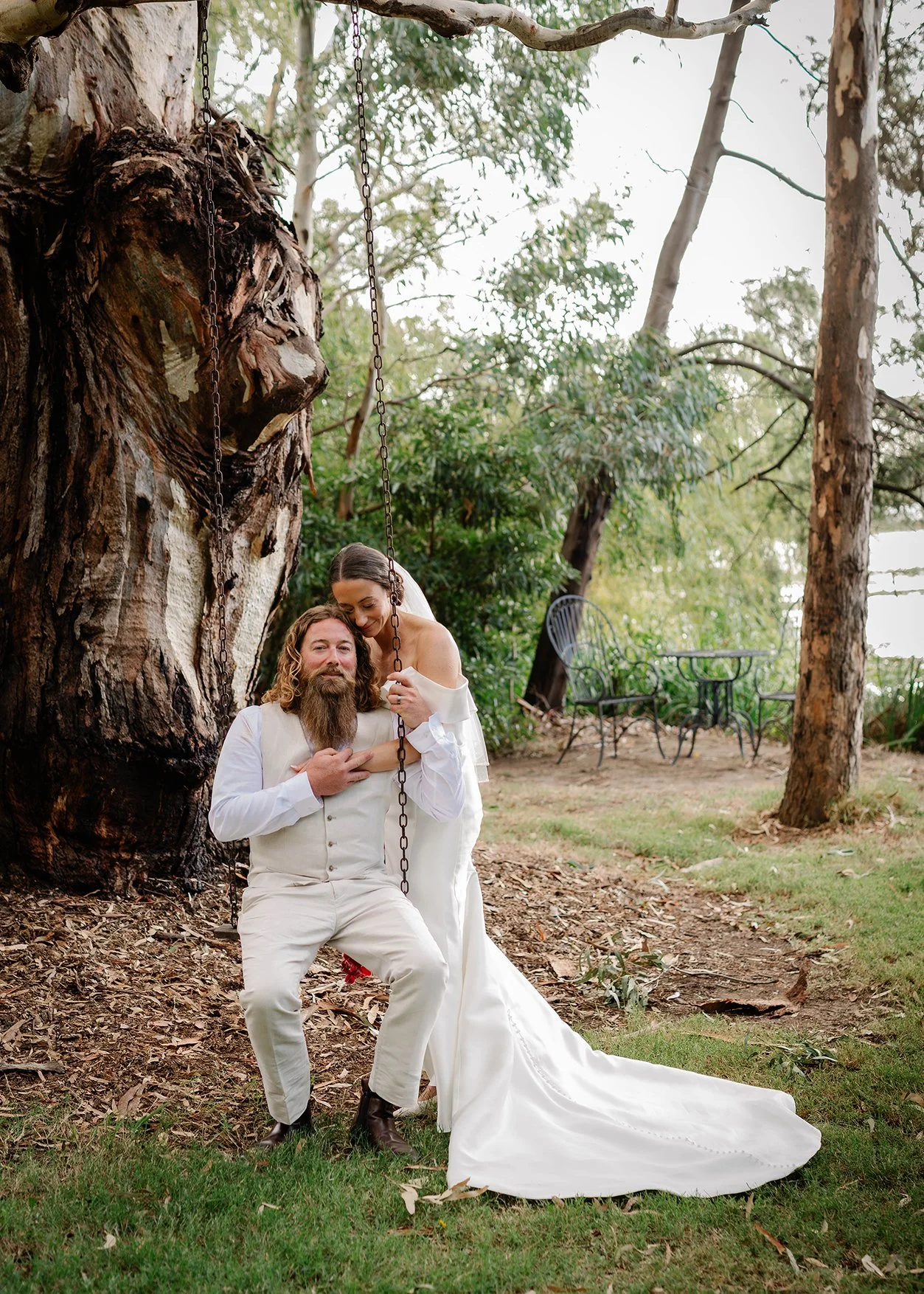 Bride and groom relaxing on a tree swing beside the water at The Boathouse Nagambie wedding venue