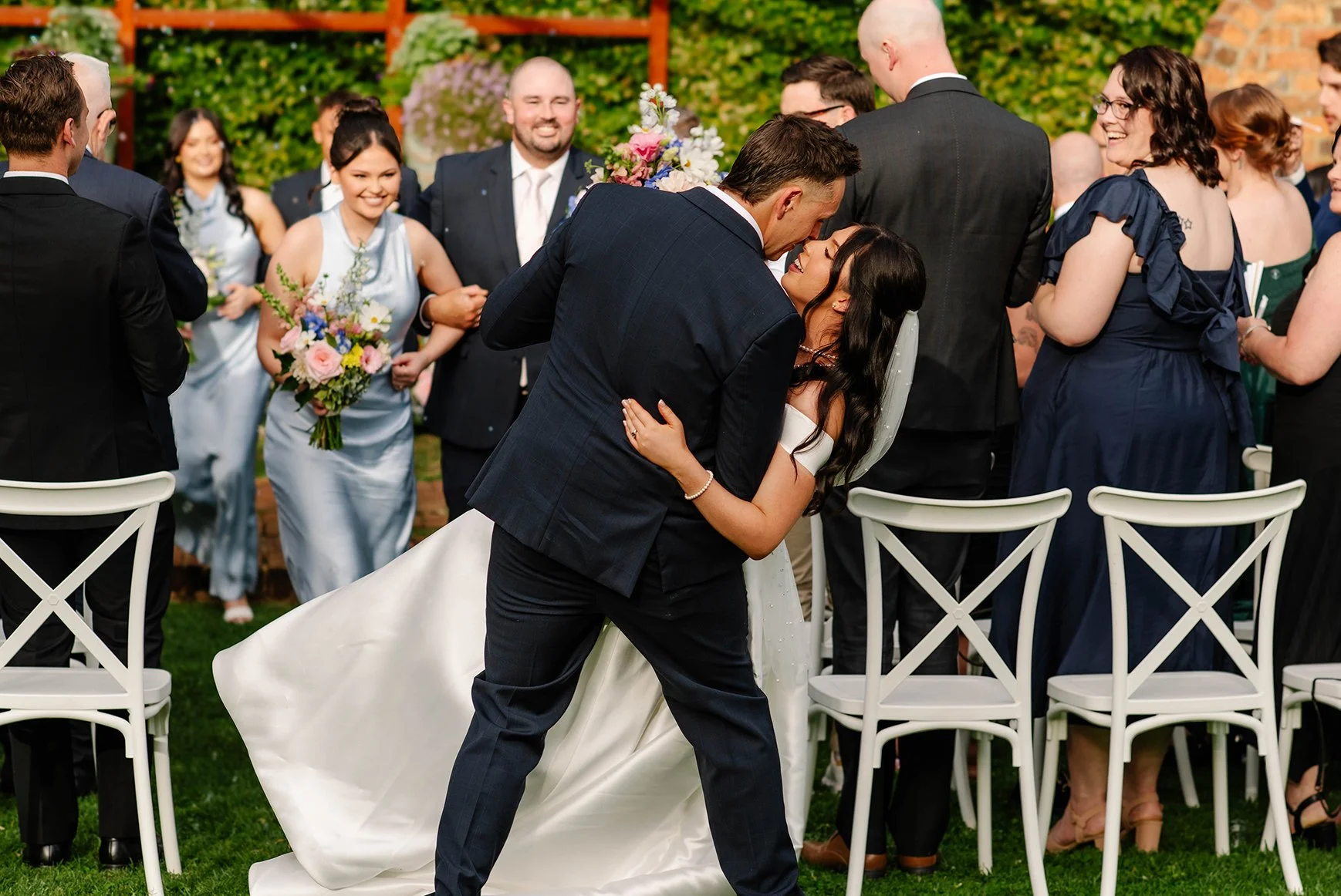 Groom dips bride back at end of aisle and gets ready to kiss her as bridal party exits behind