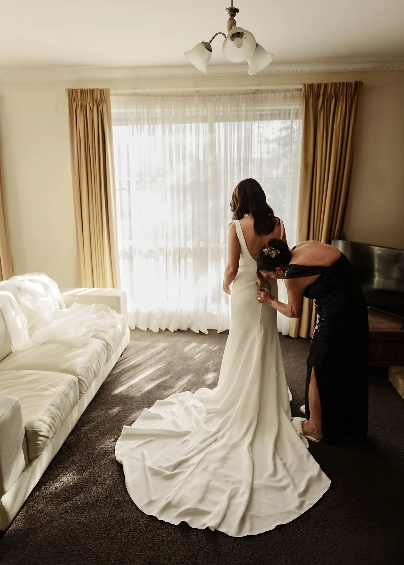 Bride being buttoned into her wedding gown by a family member in a warmly lit room at Jason's Restaurant Beaconsfield