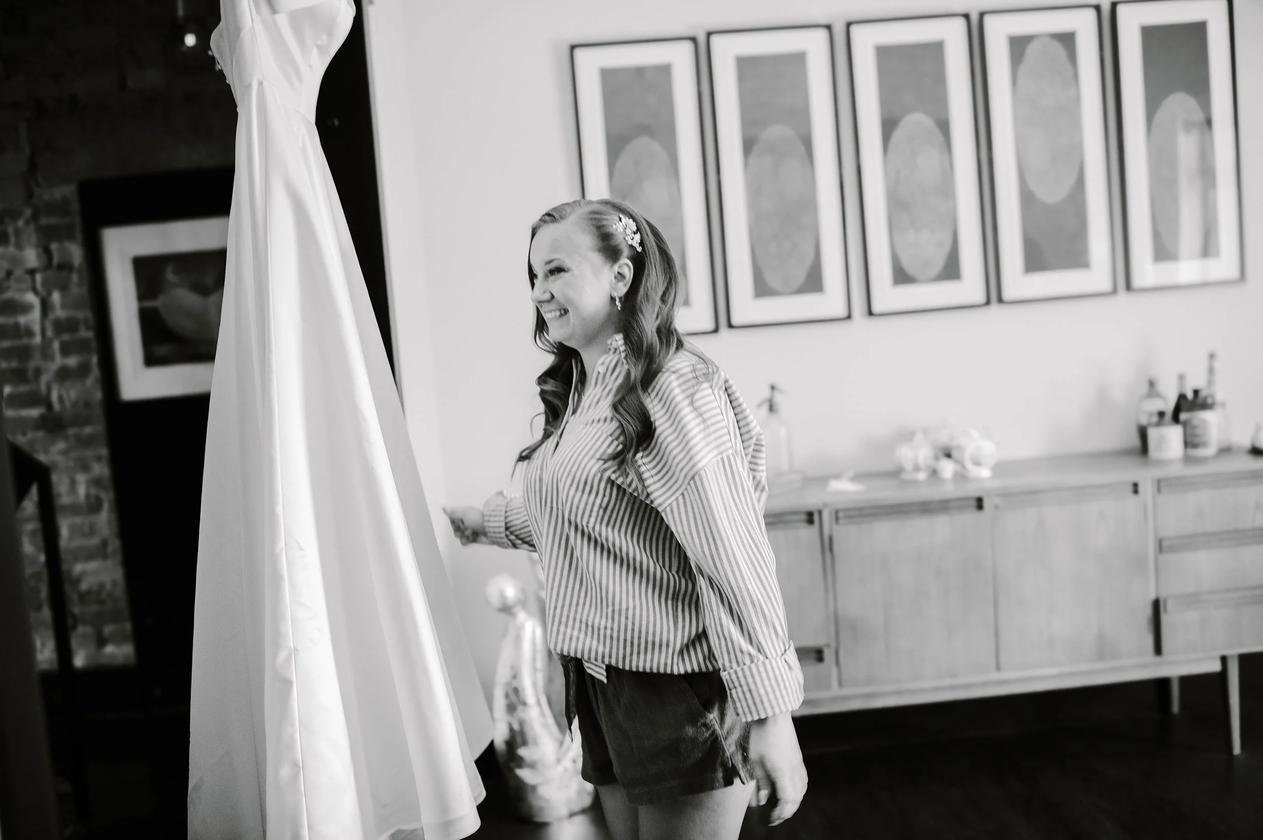 Action candid shot of bride touching her hanging wedding dress as she smiles and walks past