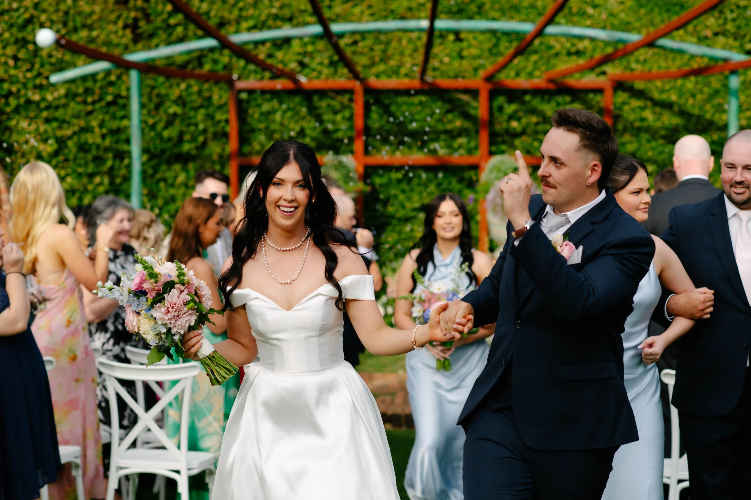 Groom holds index finger up and looks at guests as he exits the aisle and bride smiles at Cloudehill wedding