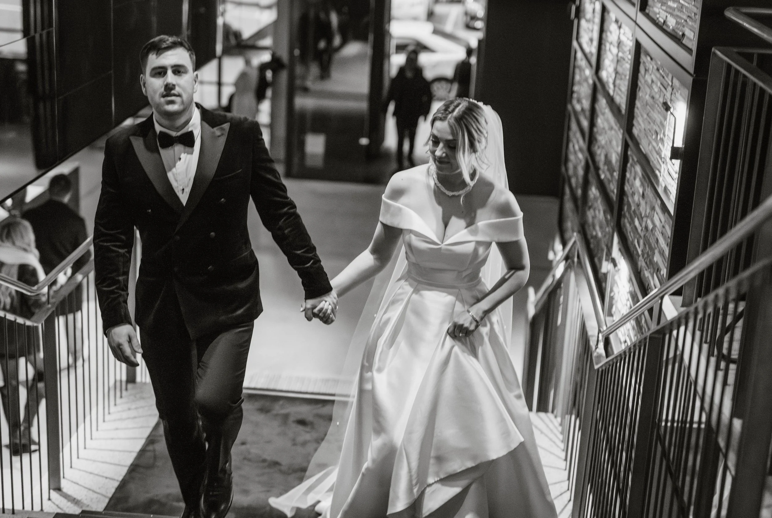 candid black and white photo of bride and groom walking up the QT Hotel Melbourne stairs