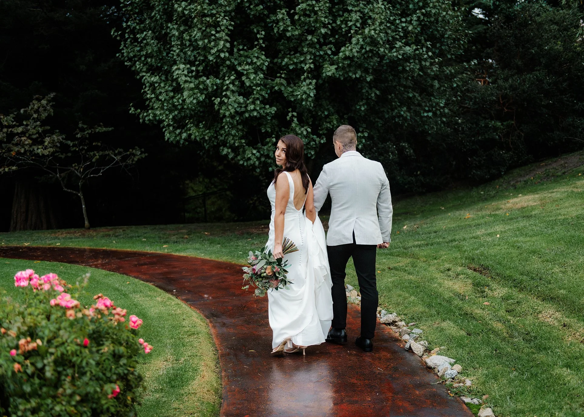 Bride looking back over her shoulder as bride and groom walk a wet garden path at Jason's Restaurant Beaconsfield Victoria