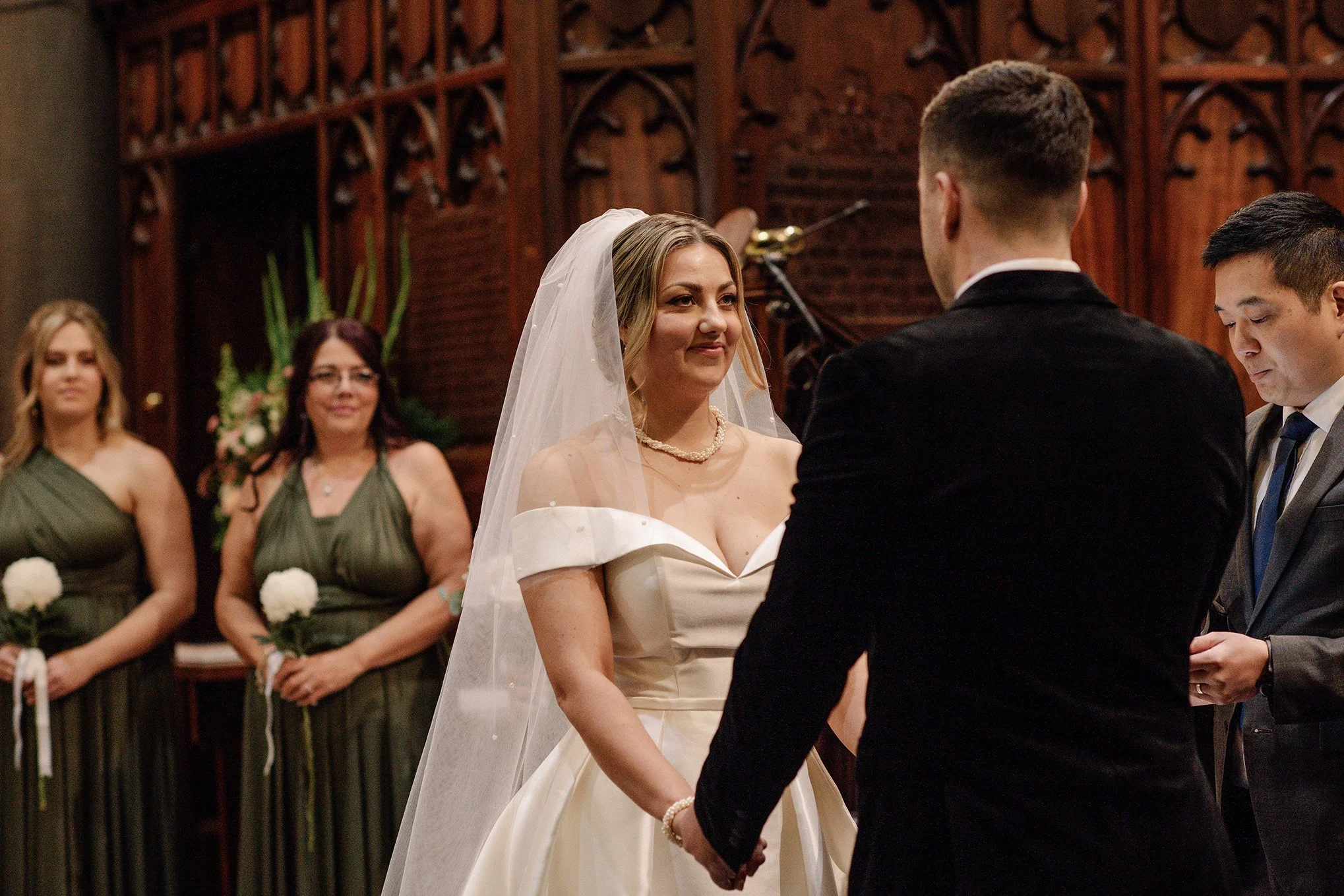 view of bride as she holds grooms hands and smiles at their church wedding ceremony in Melbourne