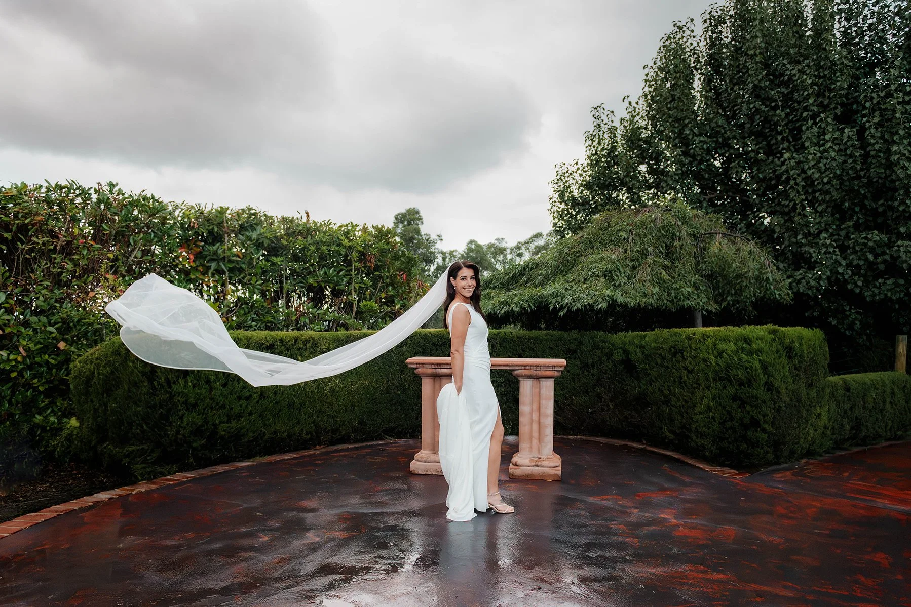 Bride smiling as her veil blows in the wind in a formal garden courtyard at Jason's Restaurant Beaconsfield Victoria