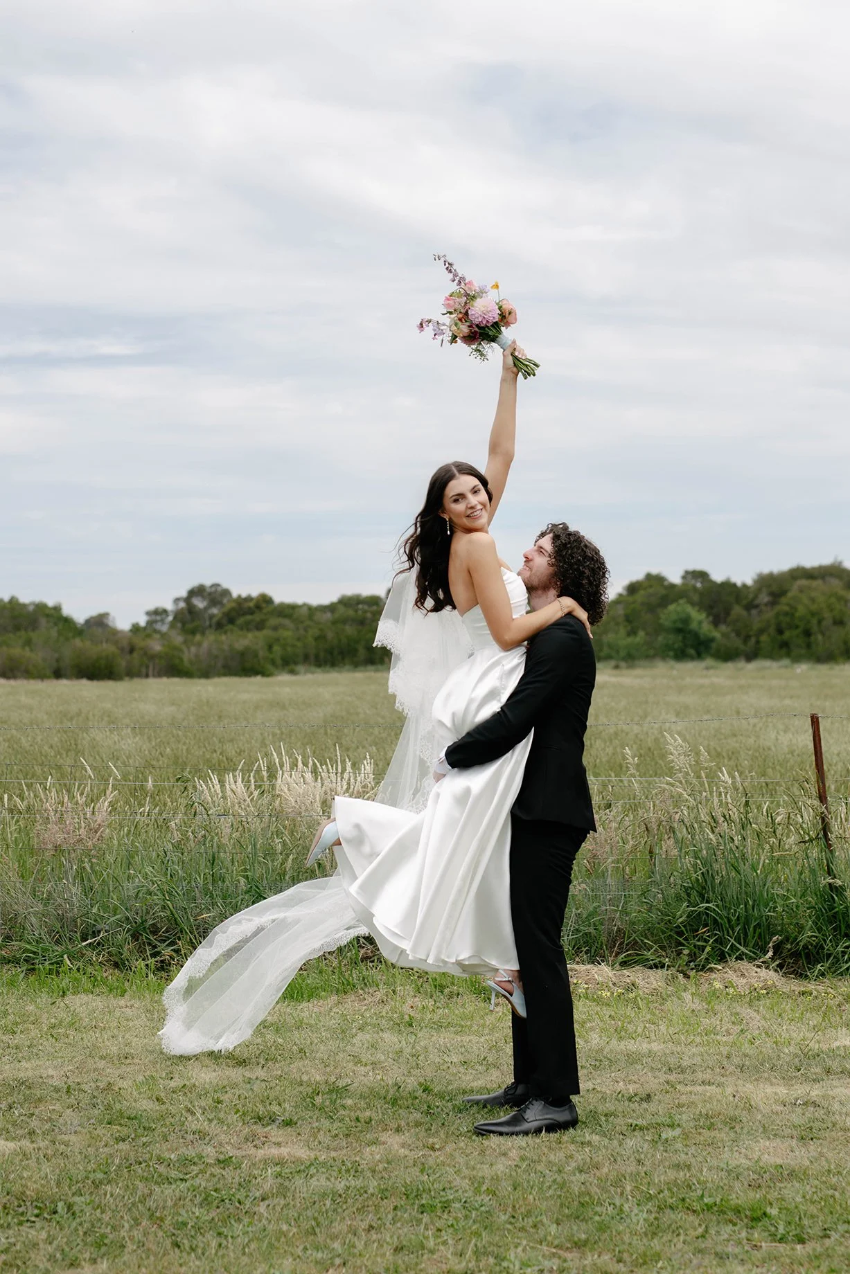 Groom lifting bride in a open paddock field at Daly Waters Rose Garden wedding venue, Victoria
