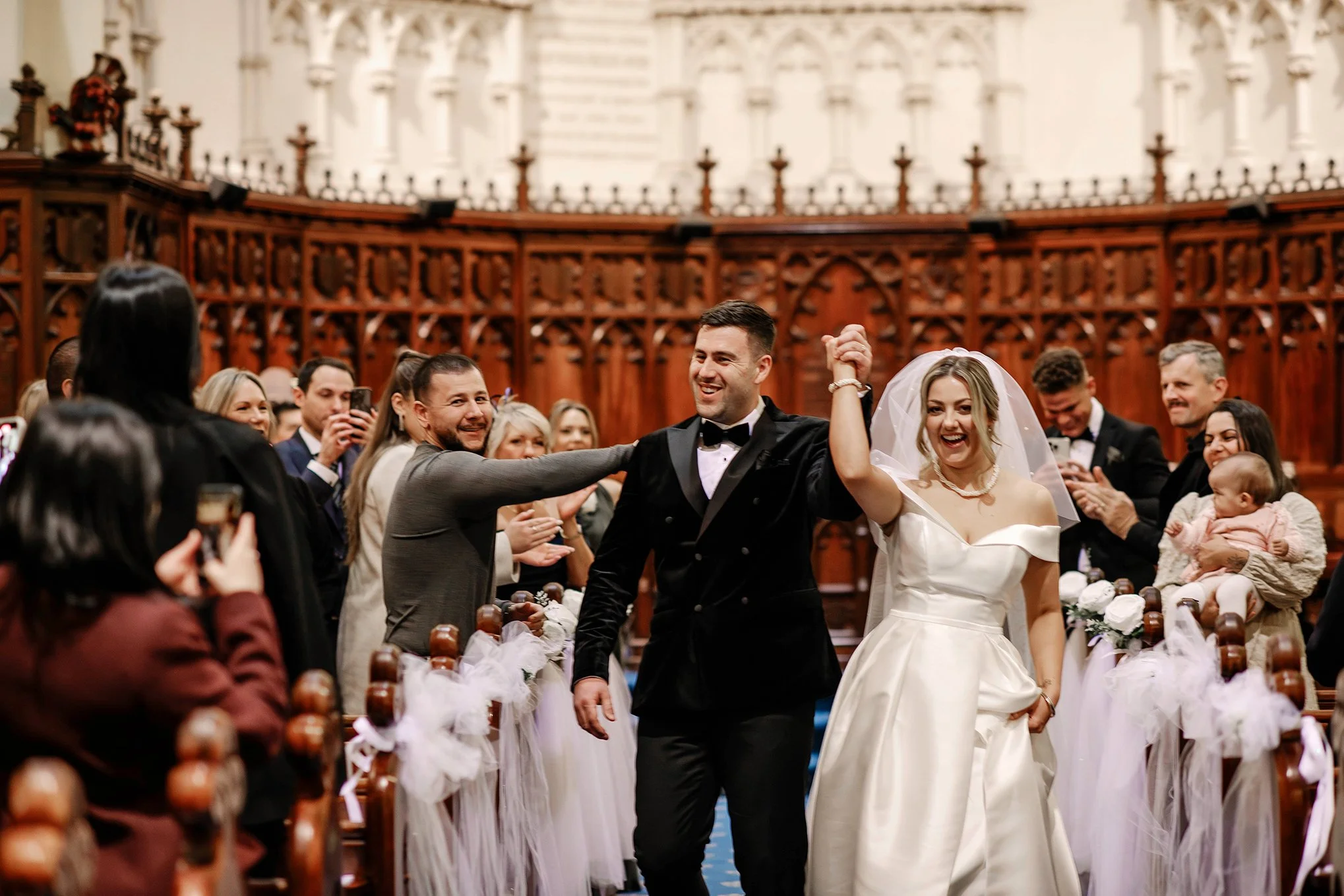 bride and groom hooray with their hands in the air as they exit down the aisle at their church wedding in Melbourne