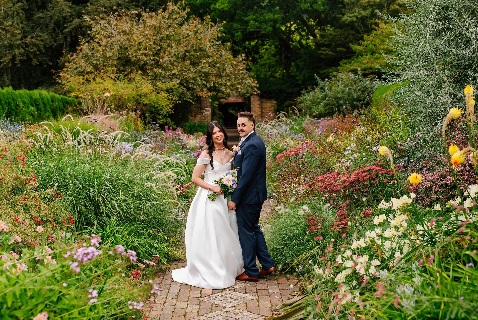 Bride and groom look back at camera after they candidly walk through the wildflower garden at Cloudehill Gardens Olinda