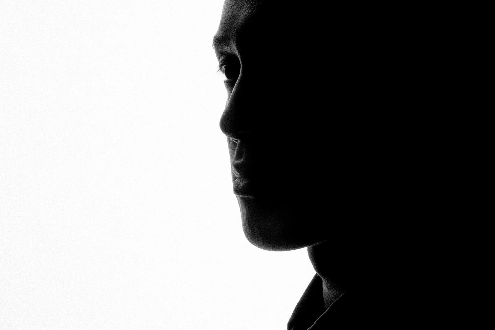 Black and white silhouette of a person's side profile with a stark contrast between light and dark areas of the face.