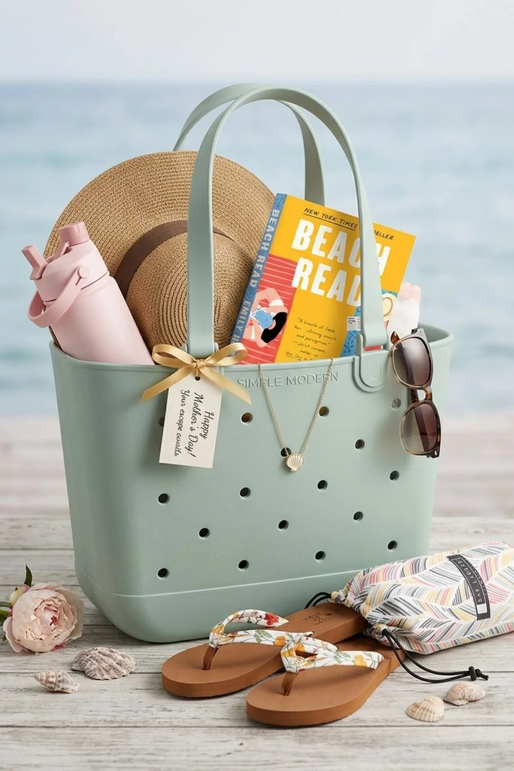 Teal rubber tote filled with beach items like a sun hat, sunglasses, water bottle, flip flops, towel, and book.
