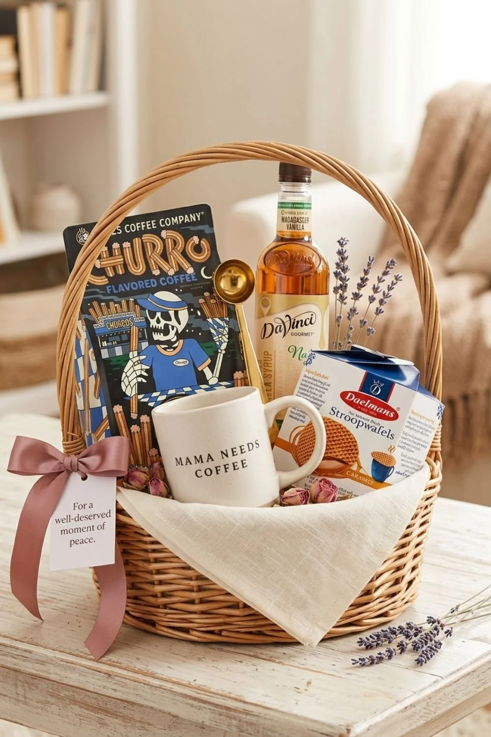 Wicker gift basket with pink bow for Mother's Day containing Churro flavored coffee, vanilla syrup, mug, coffee scoop, and Stroopwafels.
