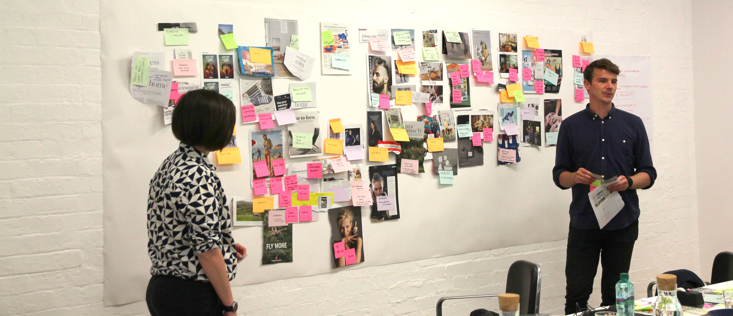 Oliver Winter facilitating a DNA workshop in front of a large wall covered with various photos, notes, and papers, in a meeting or planning session.