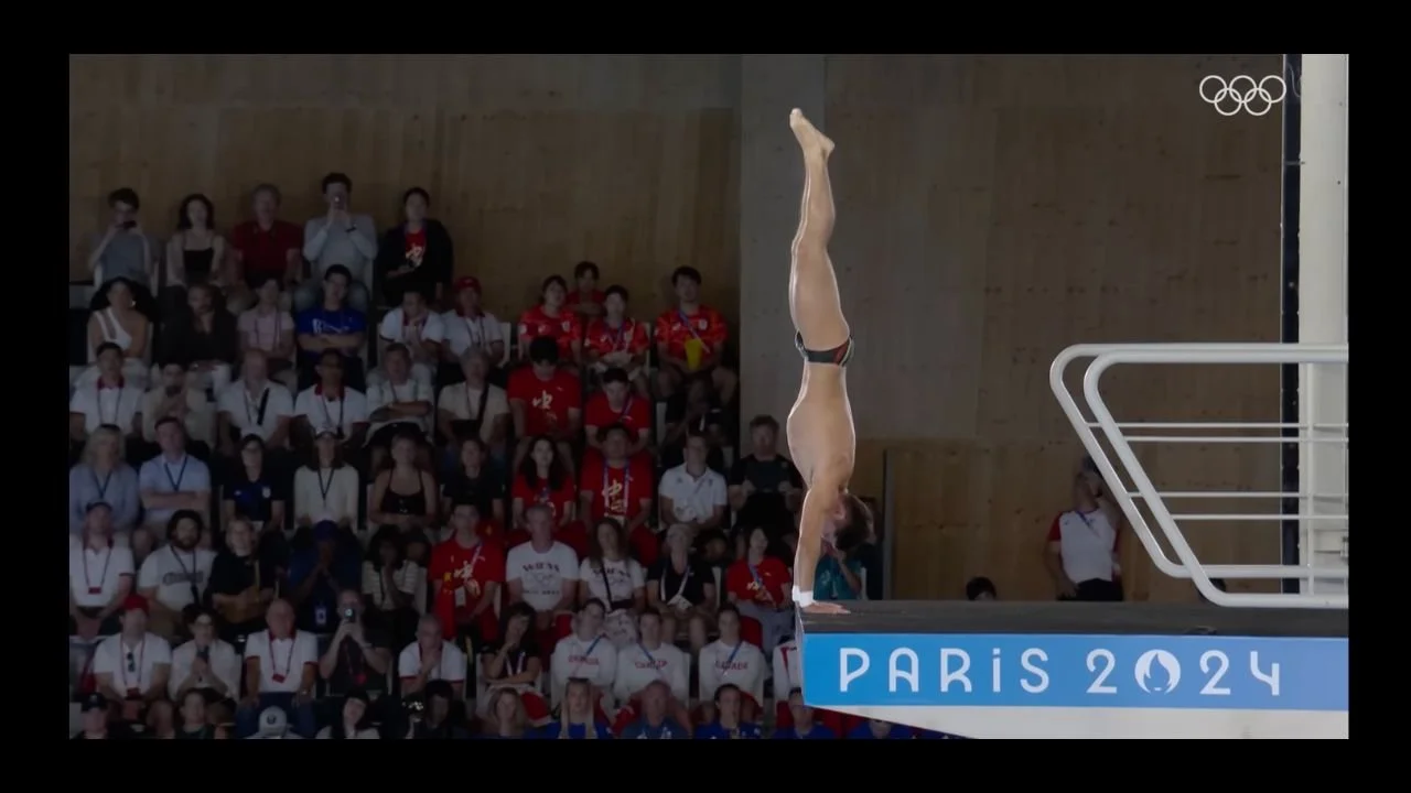 A diver doing a handstand on the 10 metre diving board, about to dive in the Paris Olympics 2024