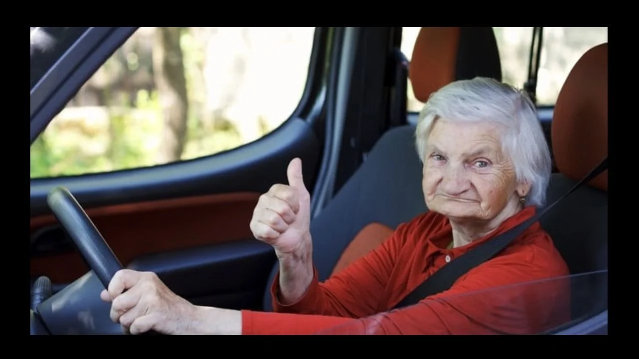 An elderly lady sitting in the driving seat giving the thumbs up sign