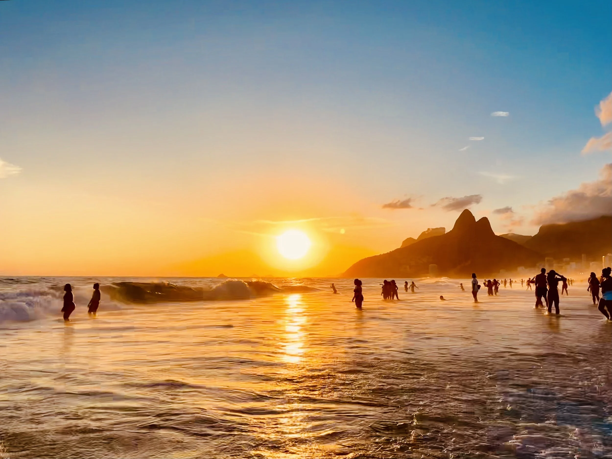 People enjoying the sunset at the beach with Rio de Janeiro's mountains in the background.
