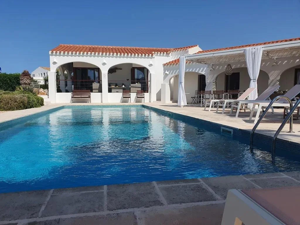 A private swimming pool with lounge chairs and a white villa with arches and red-tiled roof in the background.