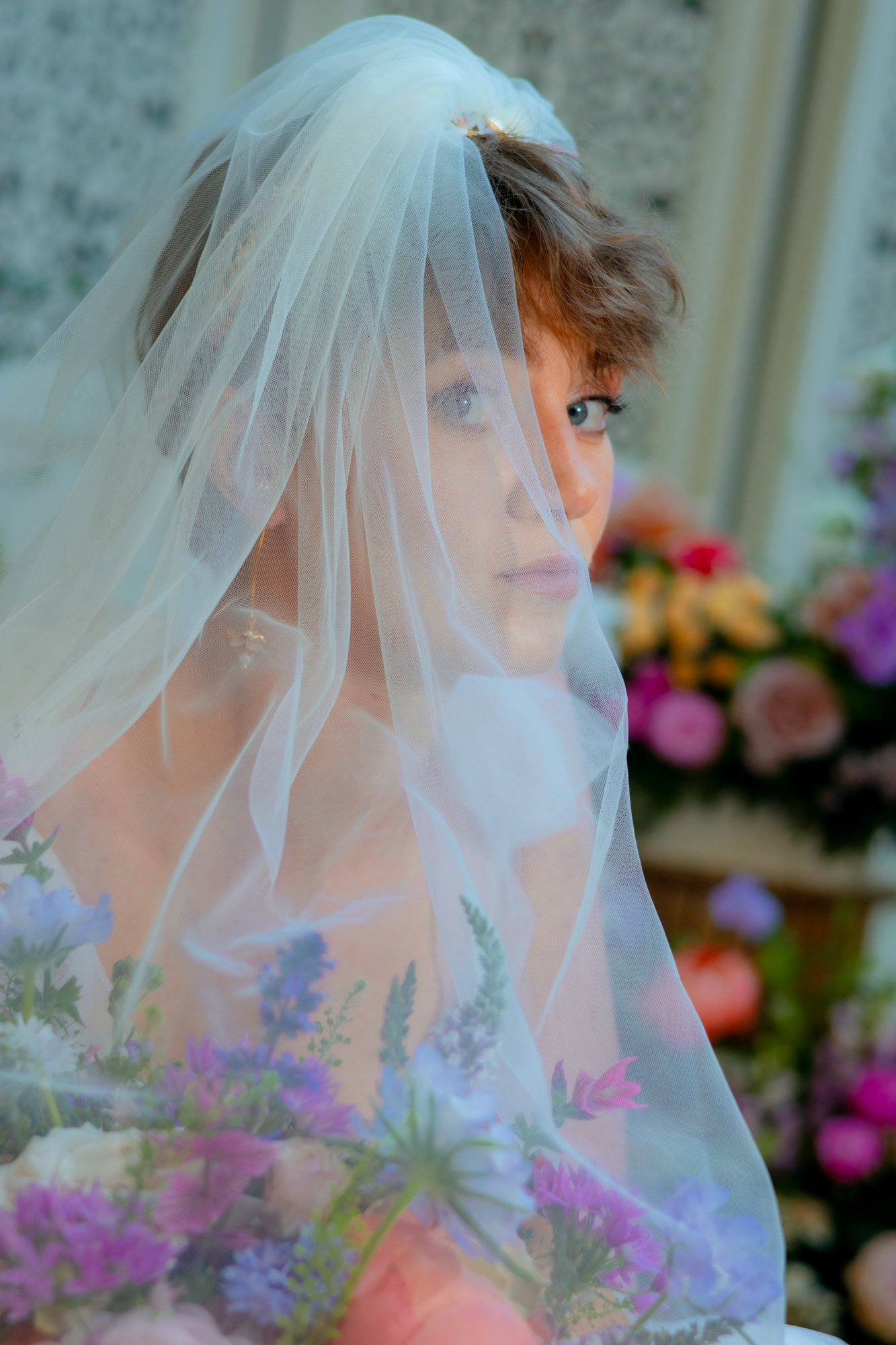 A woman with short hair wearing a veil and surrounded by flowers.
