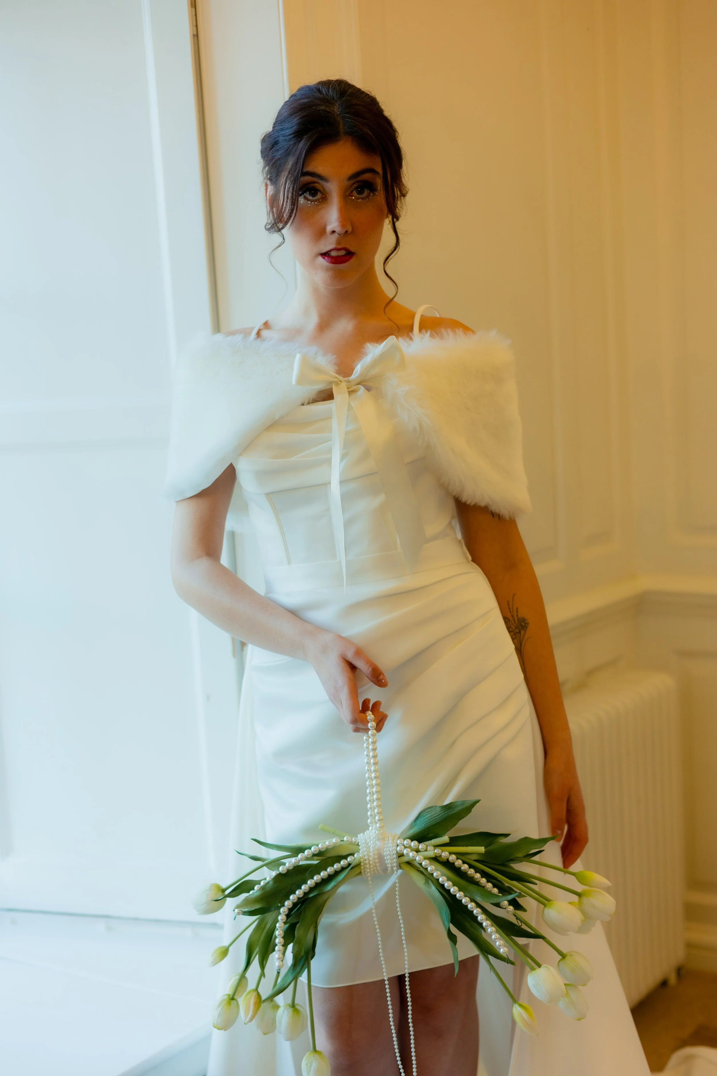 A woman in a white dress holding a pearl necklace and a bouquet of white tulips.