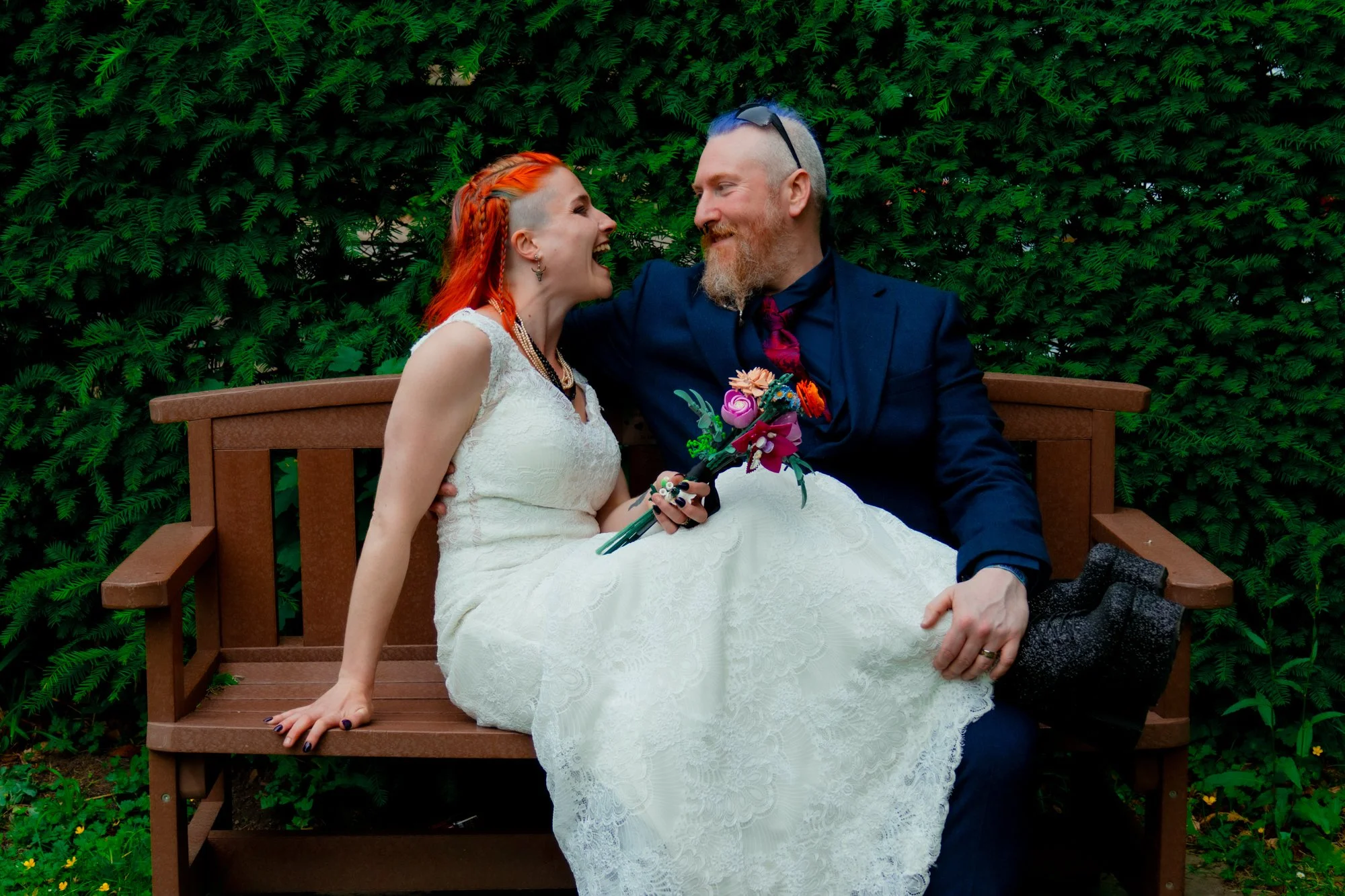 Candid wedding photography in Dorset showing couple laughing on a bench during portraits