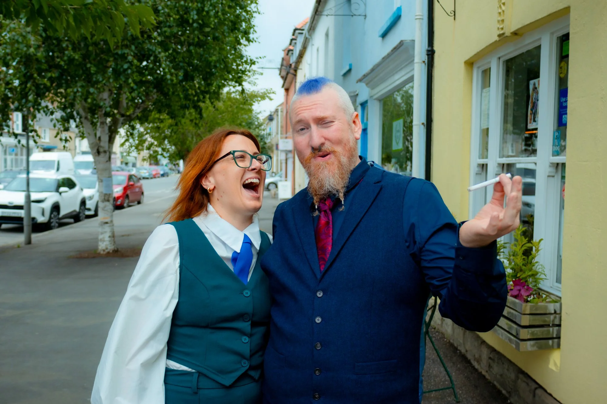 A woman and a man laughing in Bridport, Dorset and smiling on a sidewalk, during candid wedding prep portraits