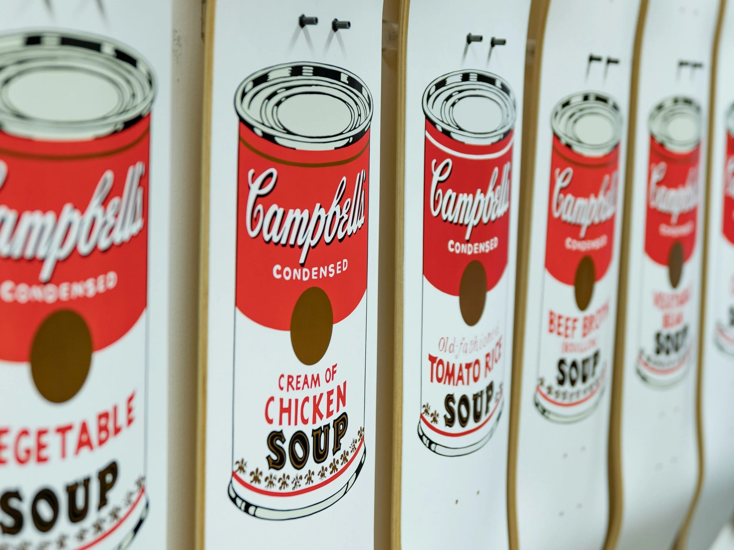A row of skateboards with Andy Warhol's Campbell's Soup art printed on them/ Photo by Photo by Jean-Philippe Delberghe on Unsplash