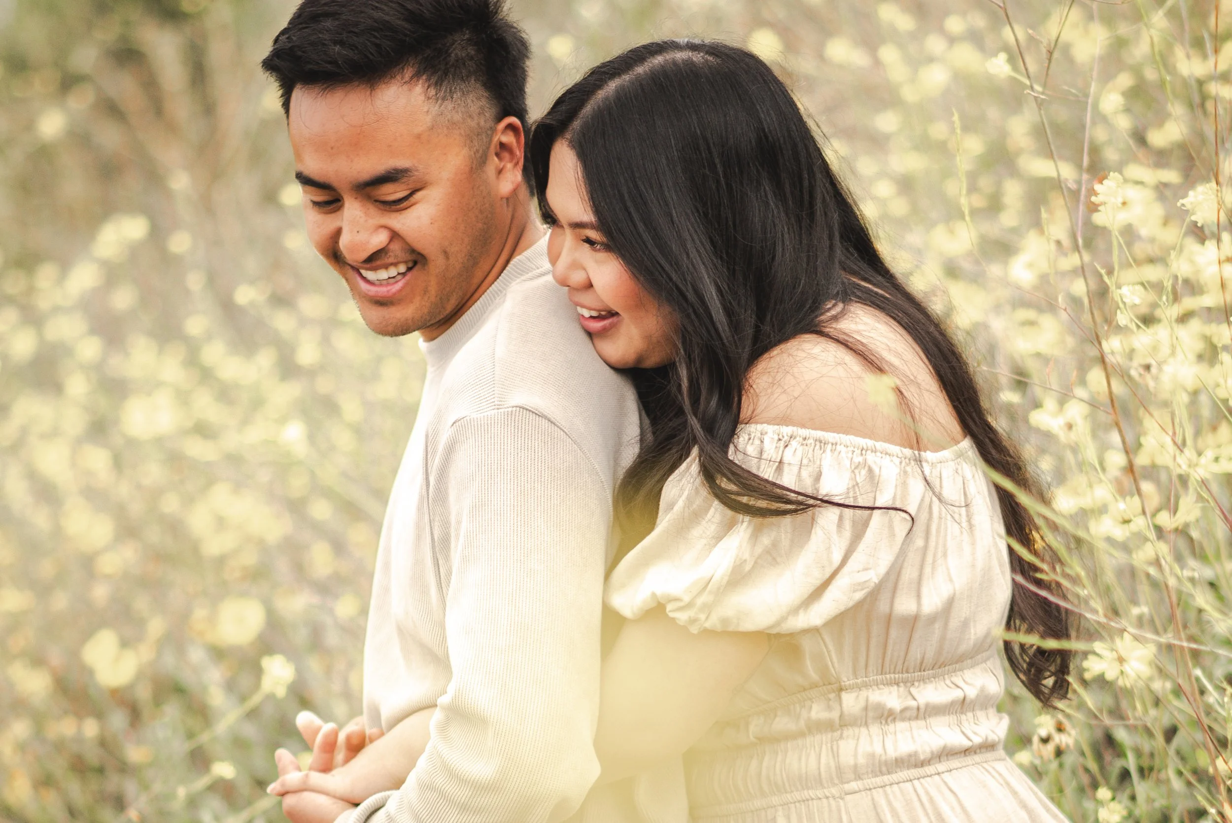 A happy couple is outdoors in a natural setting, close together, smiling and enjoying each other's company.
