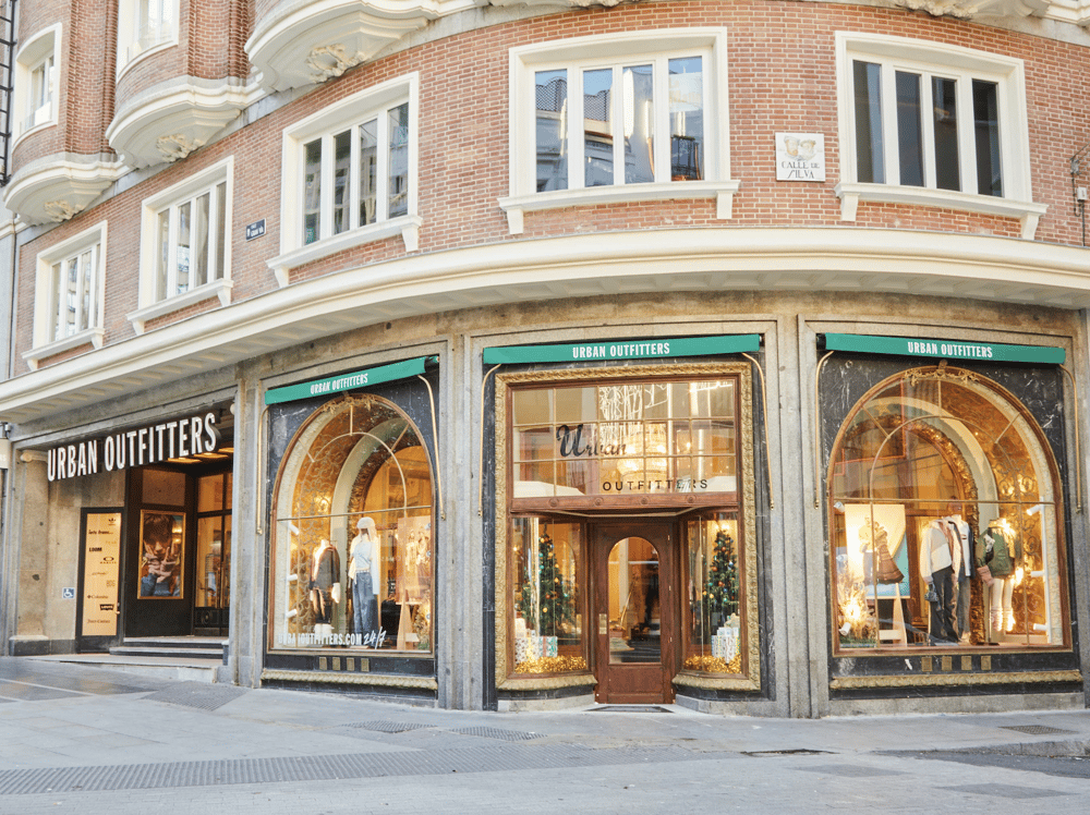 Urban Outfitters store on a city street with large storefront windows displaying mannequins dressed in casual clothing, festive decorations, and Christmas trees inside.