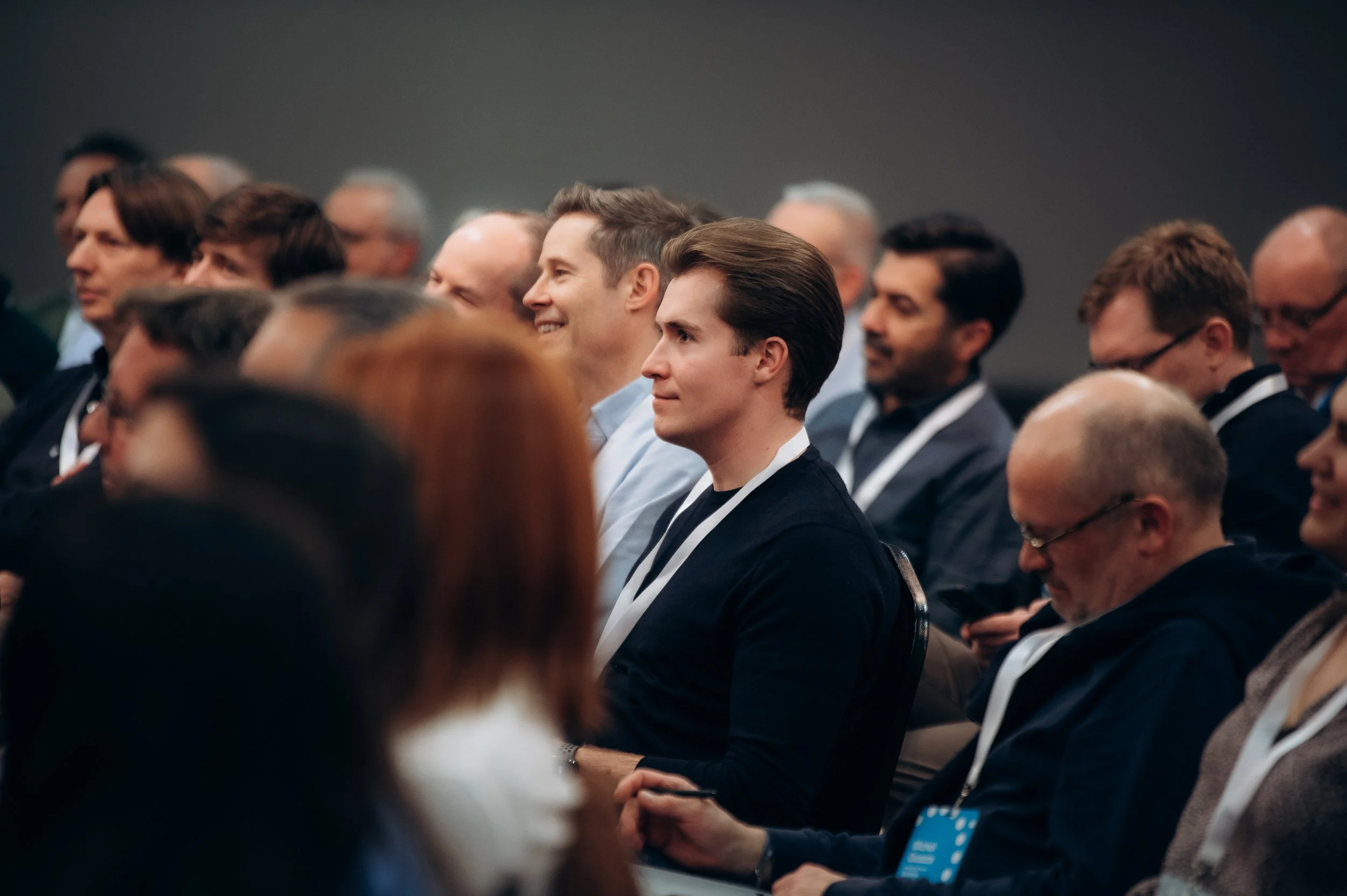 People attending a conference sitting in rows, listening and engaging with a speaker, some taking notes.