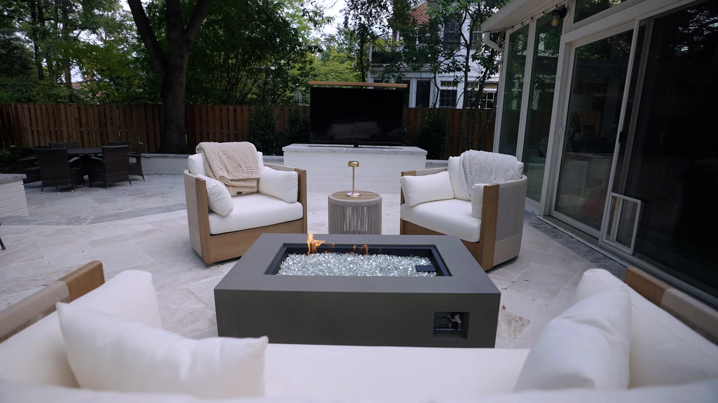 Natural stone patio with a gas fire table, lounge seating, and an outdoor TV wall in a Northern Virginia backyard