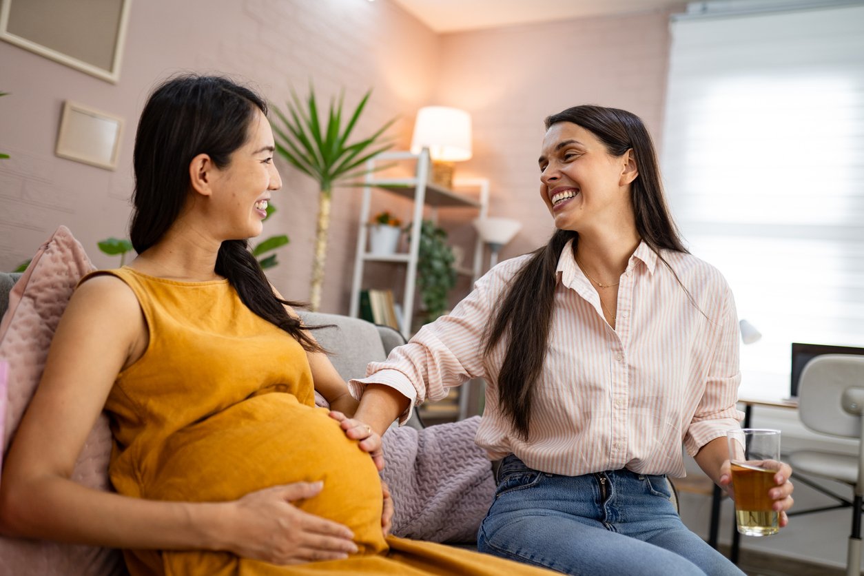 Pregnant woman talking and smiling with a supportive friend at home, illustrating emotional support during late pregnancy.