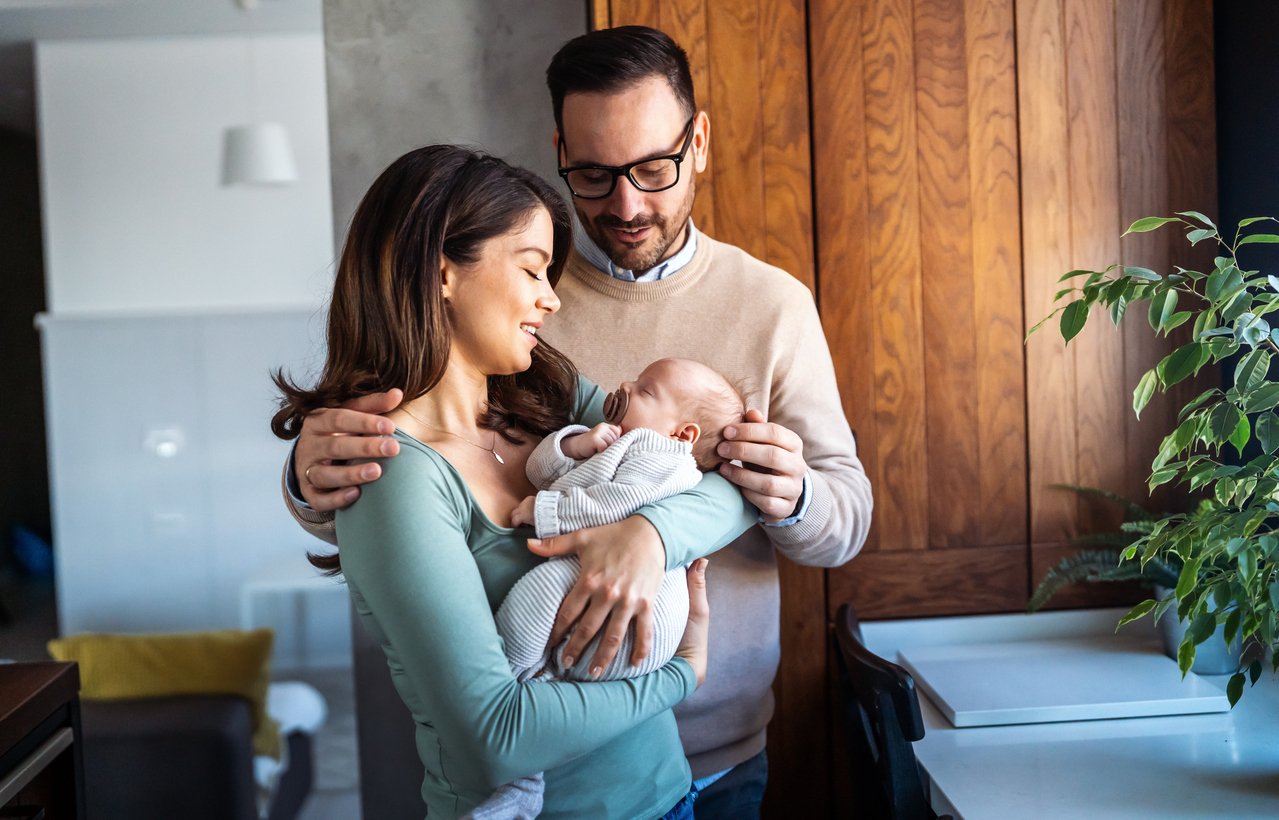 New parents holding a newborn together at home, illustrating planning for postpartum support and recovery.