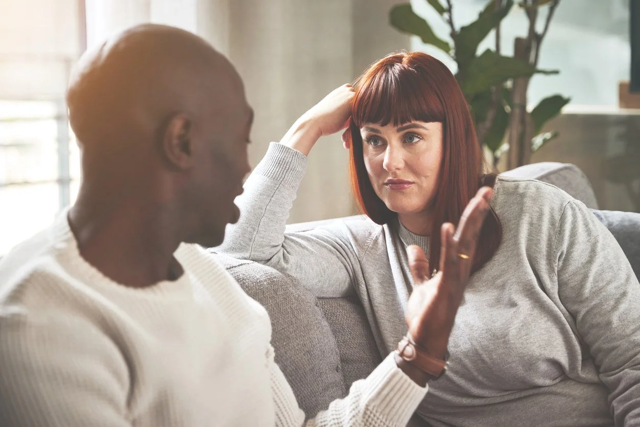 Couple on a couch having a calm, attentive conversation—one partner speaking while the other listens—introducing the love languages lens for repairing unresolved issues.