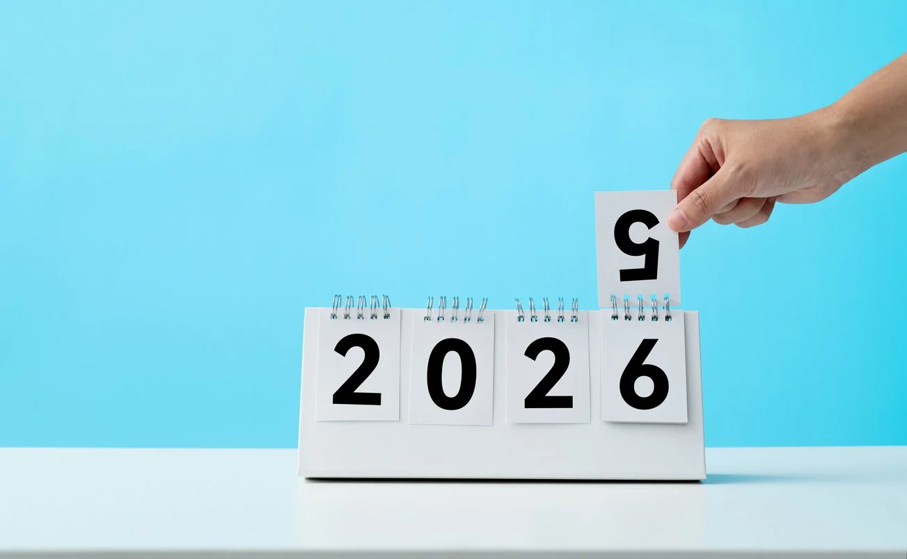 Hand flips a desk calendar from 2025 to 2026 against a blue background—symbolizing fresh starts, resolutions, and goal setting for the new year.