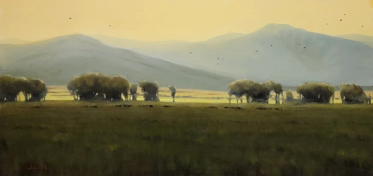 An evening scene with the cows walking home mountains in the background, trees and field in foreground.