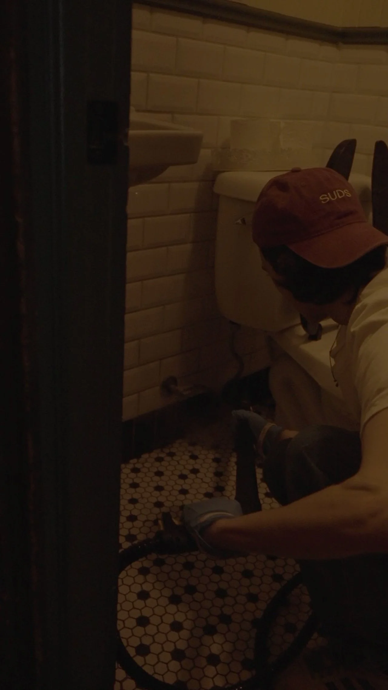 A person working on a toilet in a dimly lit bathroom.