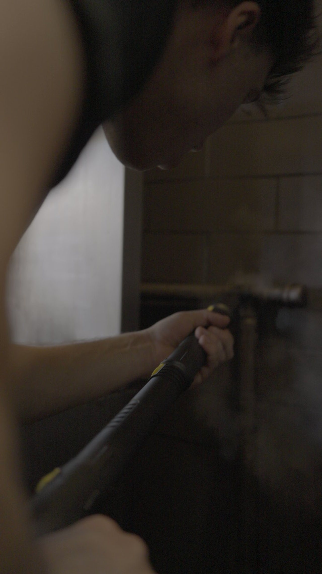 A person is laying on the ground, holding a flashlight, in a dark and cramped space with wooden walls.