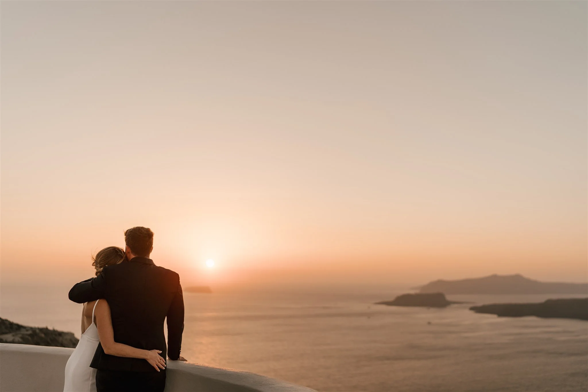 Newlywed couple overlooking the Aegean Sea at sunset during their destination wedding in Santorini, Greece