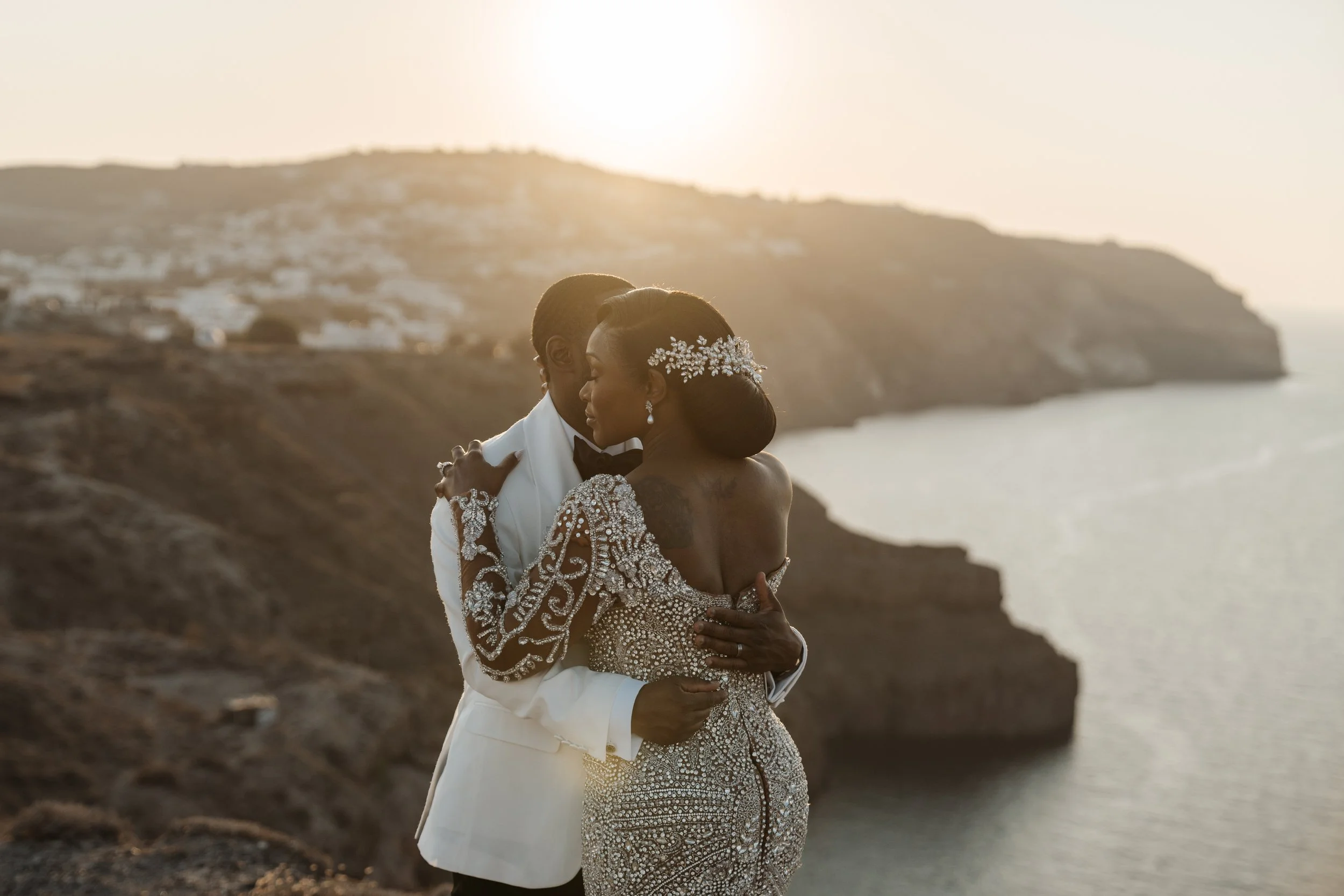Newlyweds embracing at sunset on the Santorini caldera, with the bride wearing an intricately beaded wedding gown.