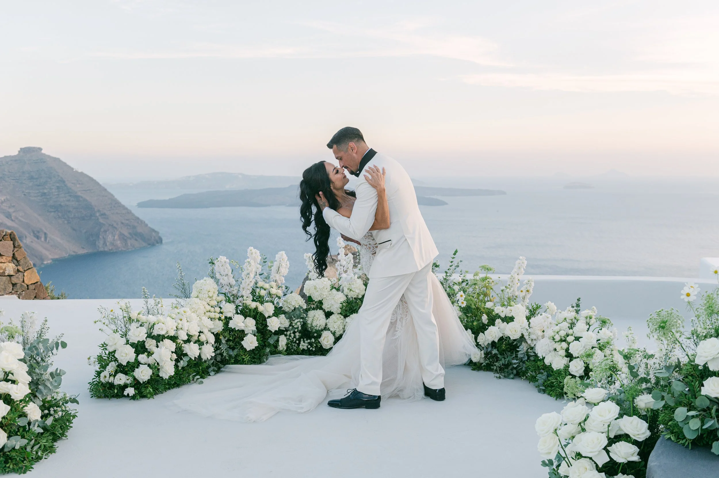 Bride and groom surrounded by white flowers at their luxury wedding overlooking the Santorini caldera in Greece